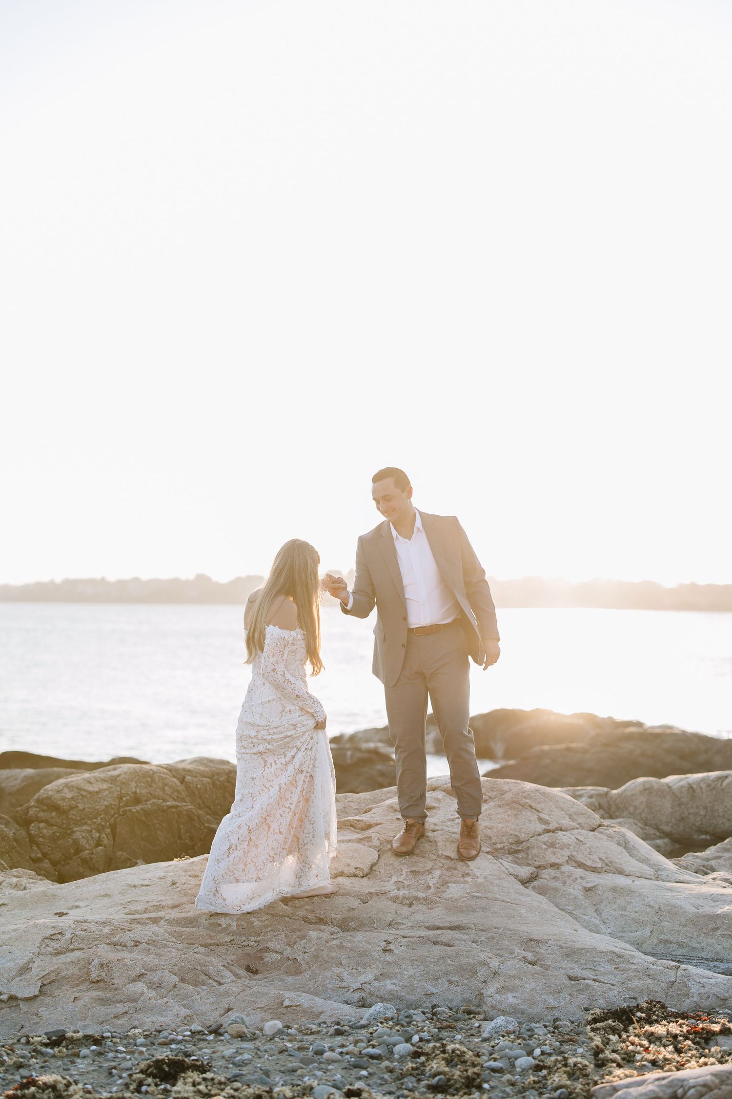 Couple standing together on rocky coastal outcrop at golden hour.