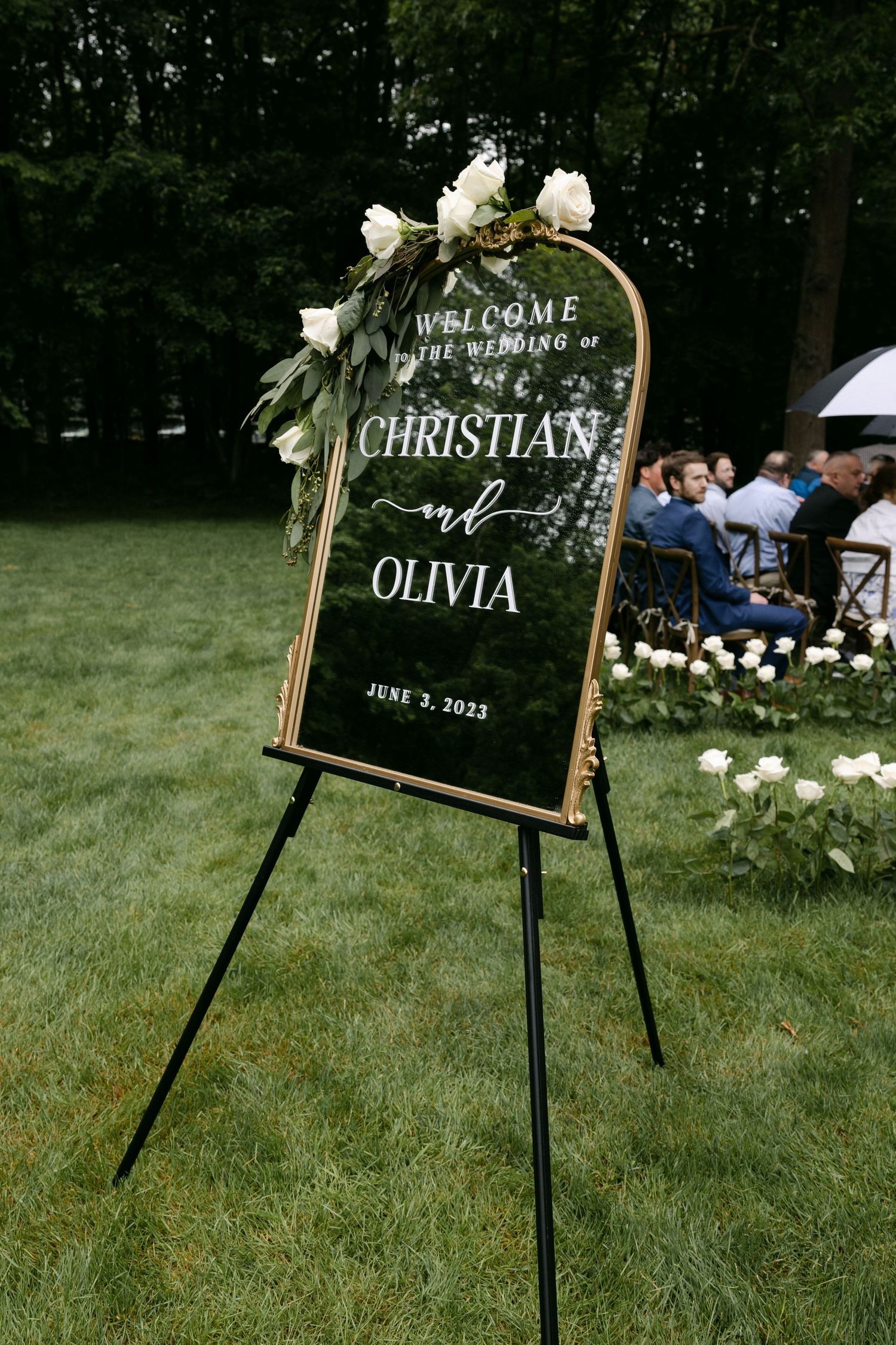 Elegant wedding welcome sign decorated with white flowers stands on grass.