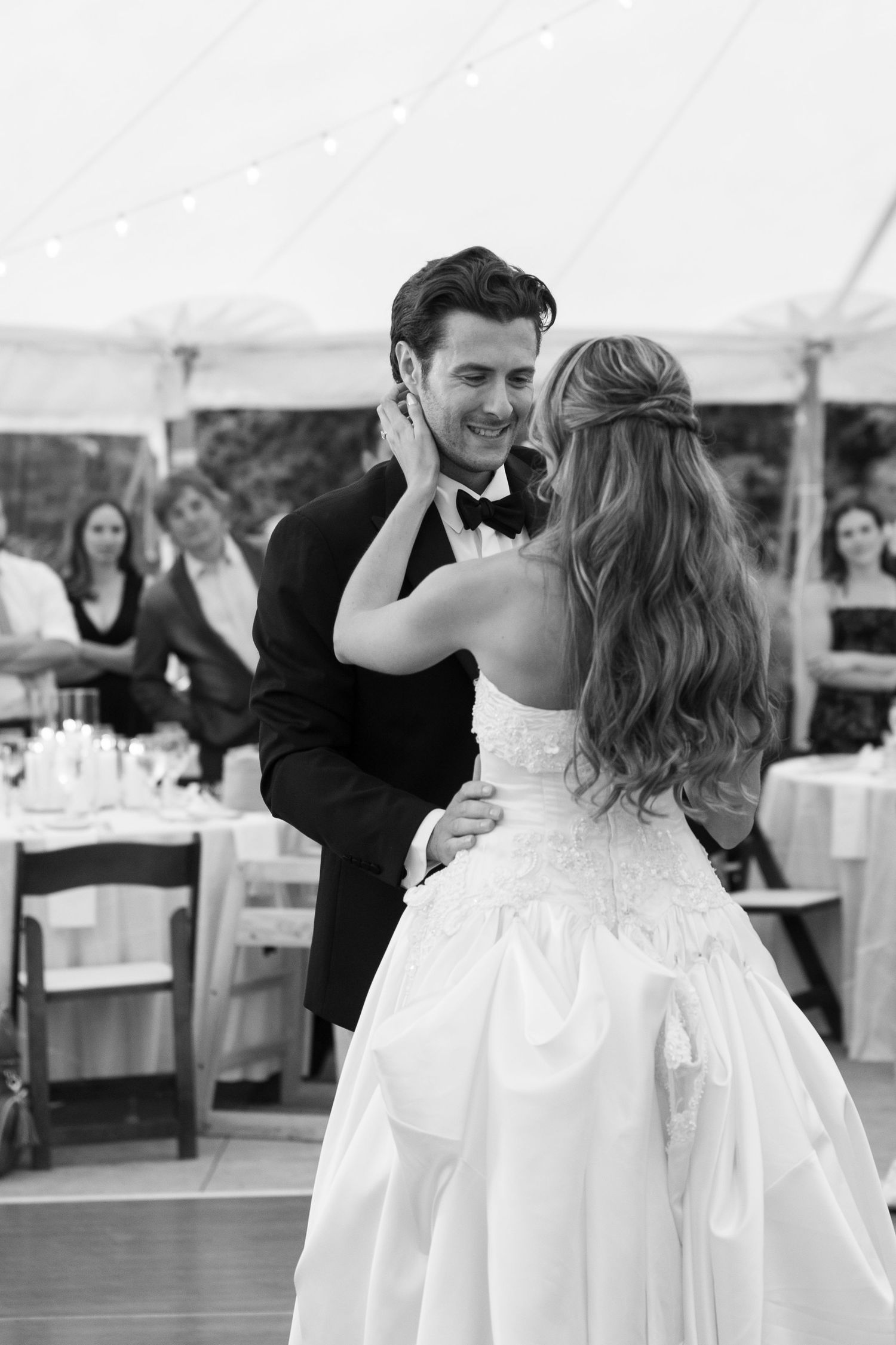 A couple shares their first dance under a white tent reception with elegant table settings.