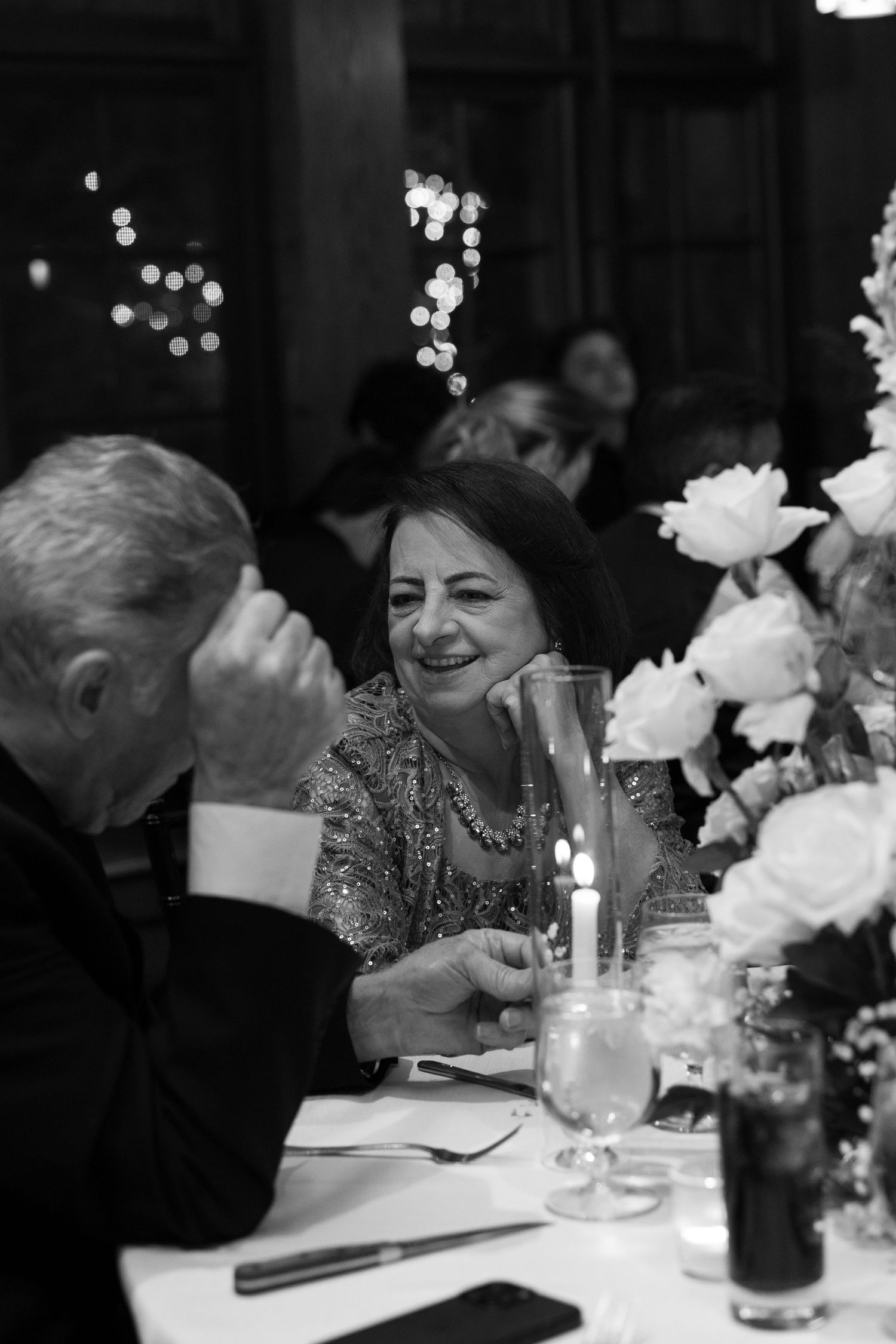 Wedding guests enjoying a formal dinner reception with white floral centerpieces and glassware on elegantly set tables.