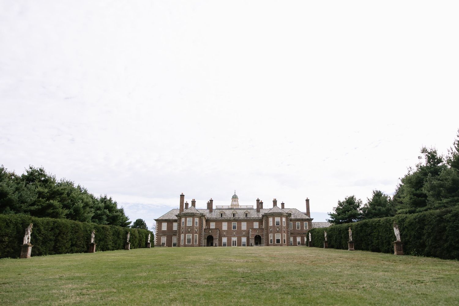 A stately mansion with manicured grounds viewed from across a vast green lawn.