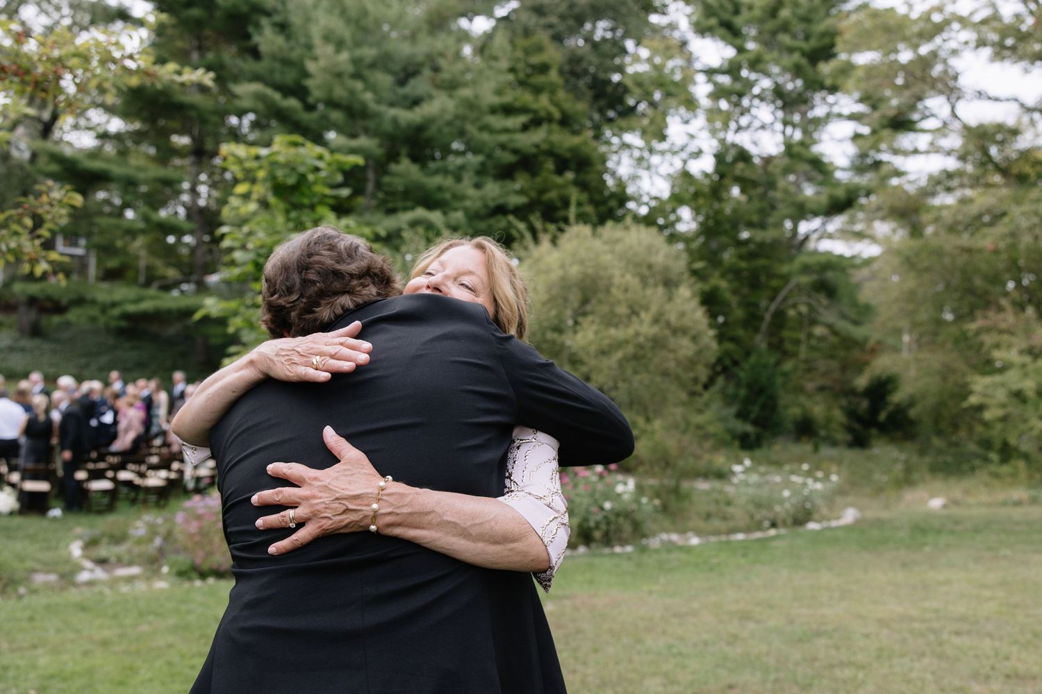 An emotional embrace is shared during an outdoor wedding with pine trees in the background.