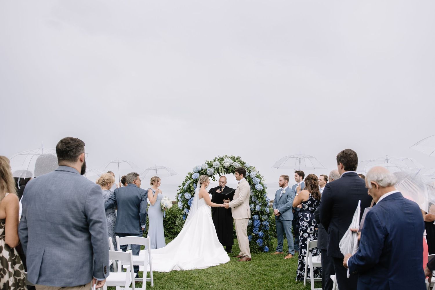 Wedding guests gather on a lawn for an outdoor ceremony under overcast skies.