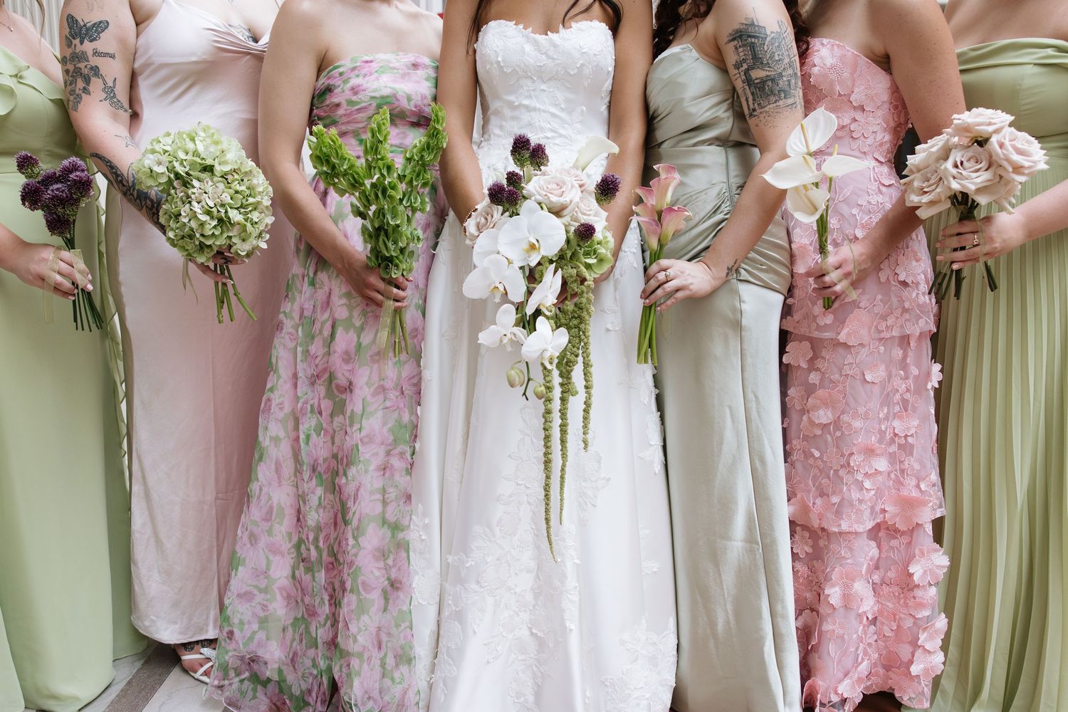 Bride in white gown with bridesmaids in pink and green dresses holding floral bouquets at a wedding.