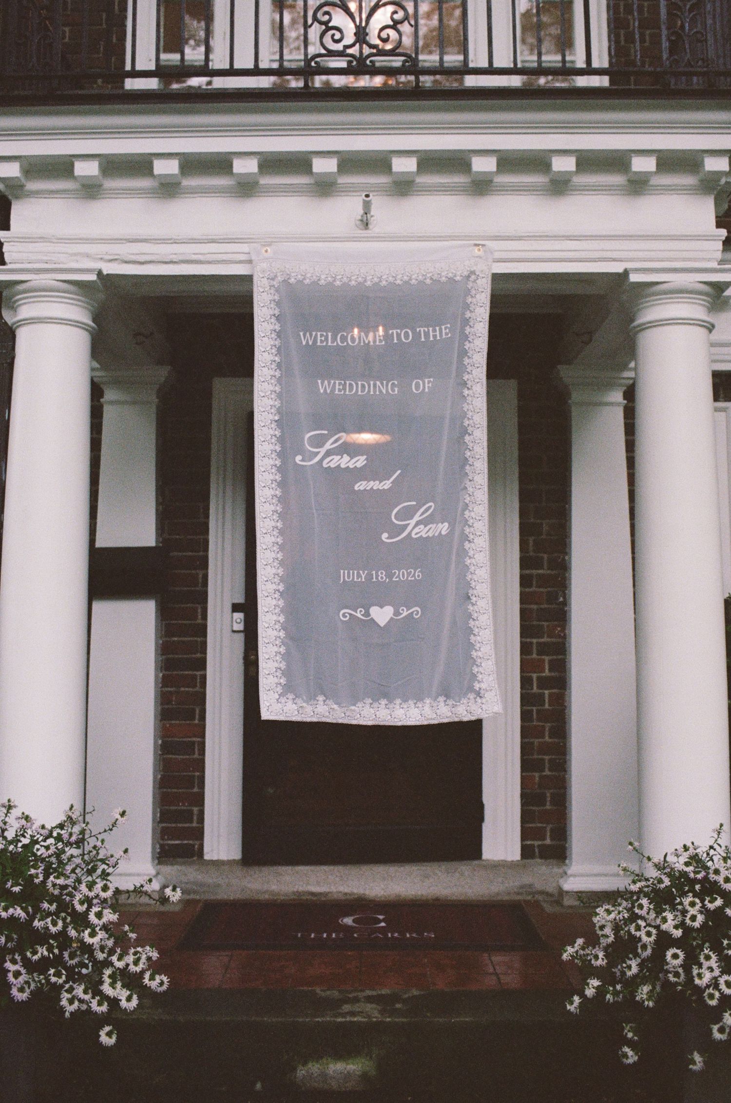 Wedding banner reading Welcome to the Wedding of Sara and Sean July 19, 2026 hanging on elegant white columned entrance.