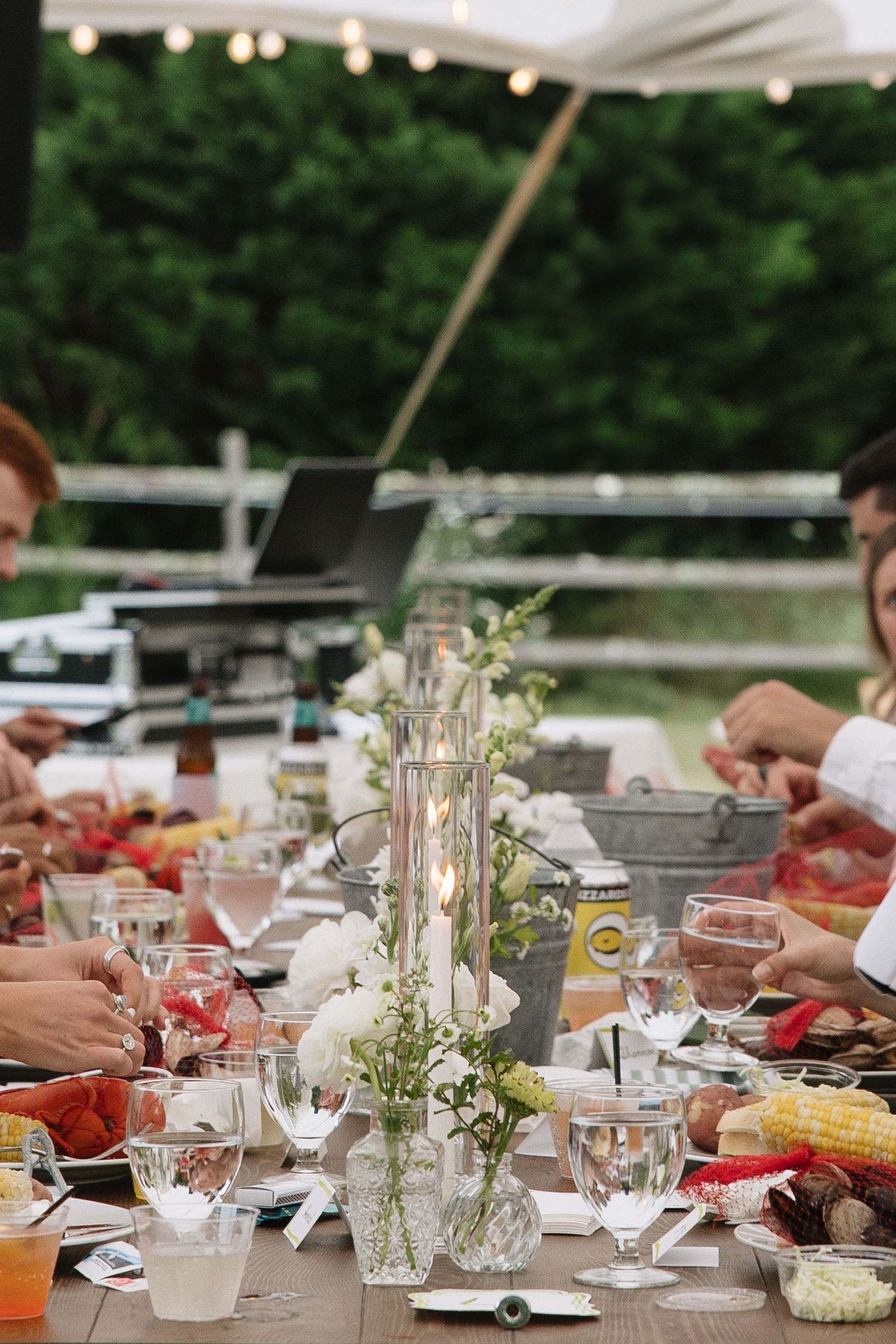 Elegant outdoor dinner party table set with candles, white flowers, wine glasses, and seafood dishes under a tent.