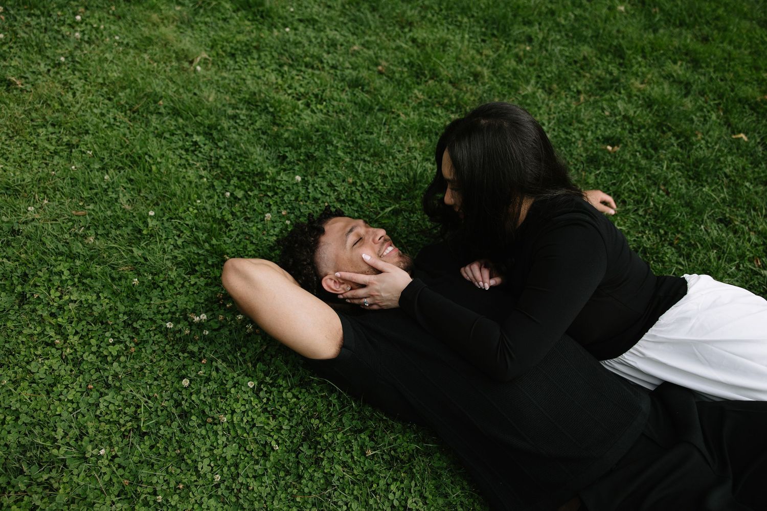 Two people sharing an intimate moment while lying on grass outdoors.