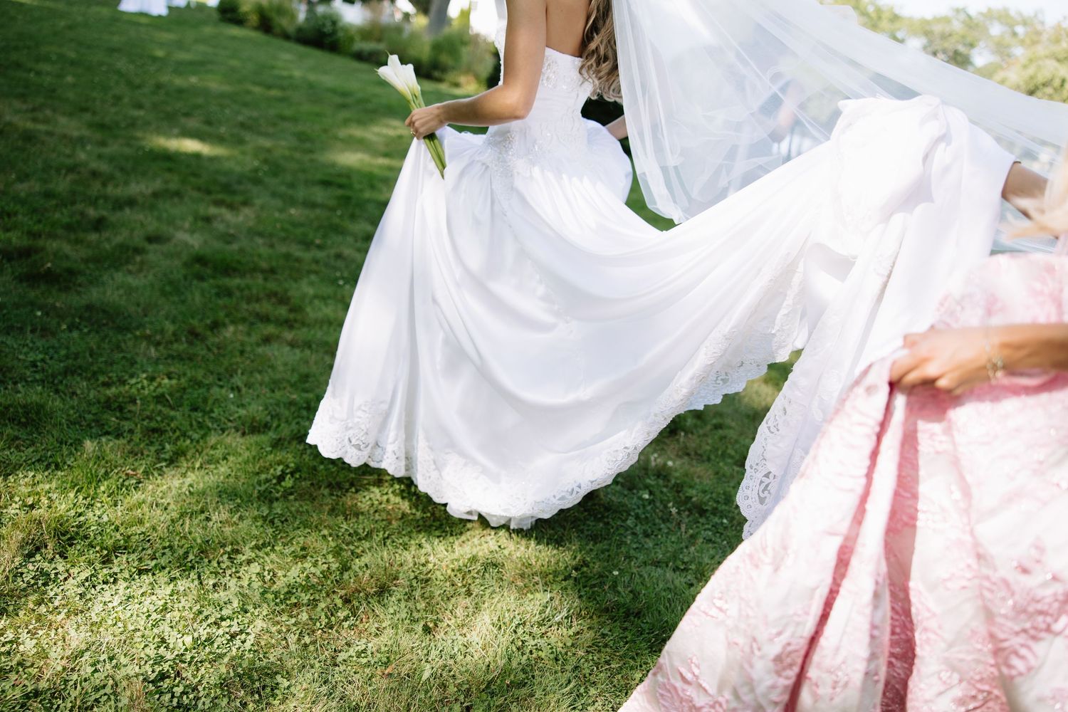 White wedding dress and pink bridesmaid dress flowing on sunny grass lawn.