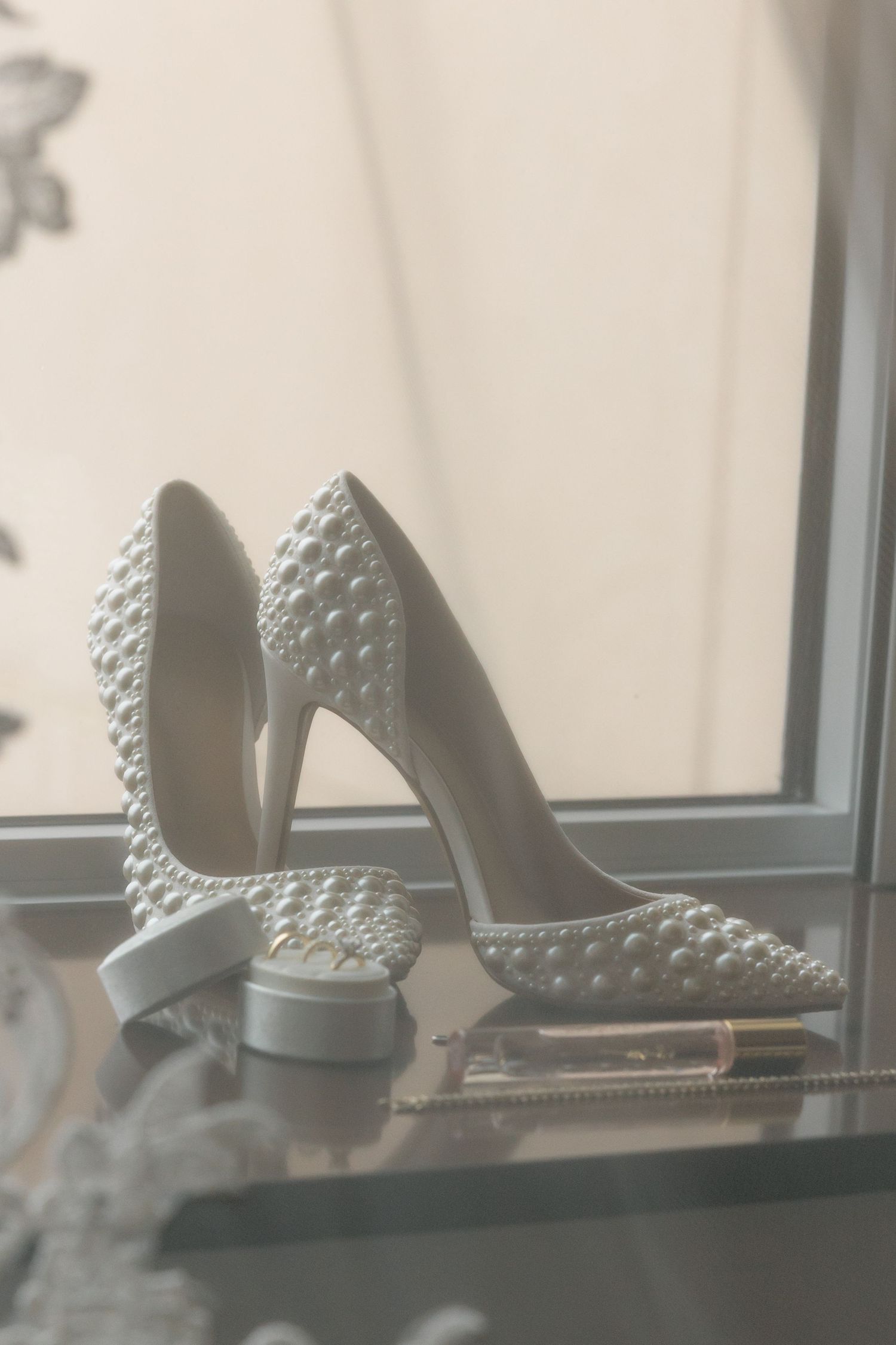 Elegant white bridal heels decorated with pearl embellishments displayed near a window.