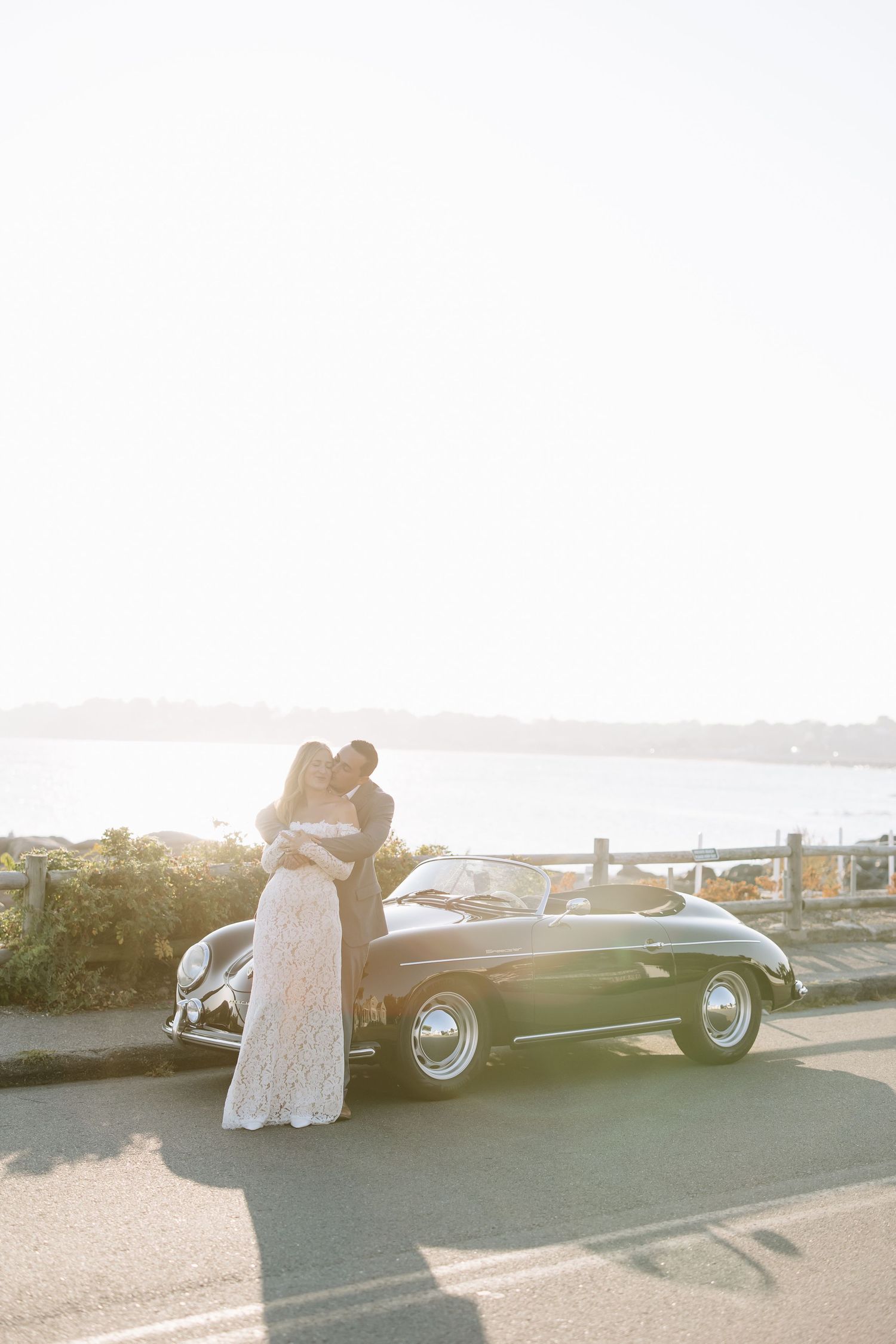 A classic black vintage car parked at sunset with blurred figures nearby.