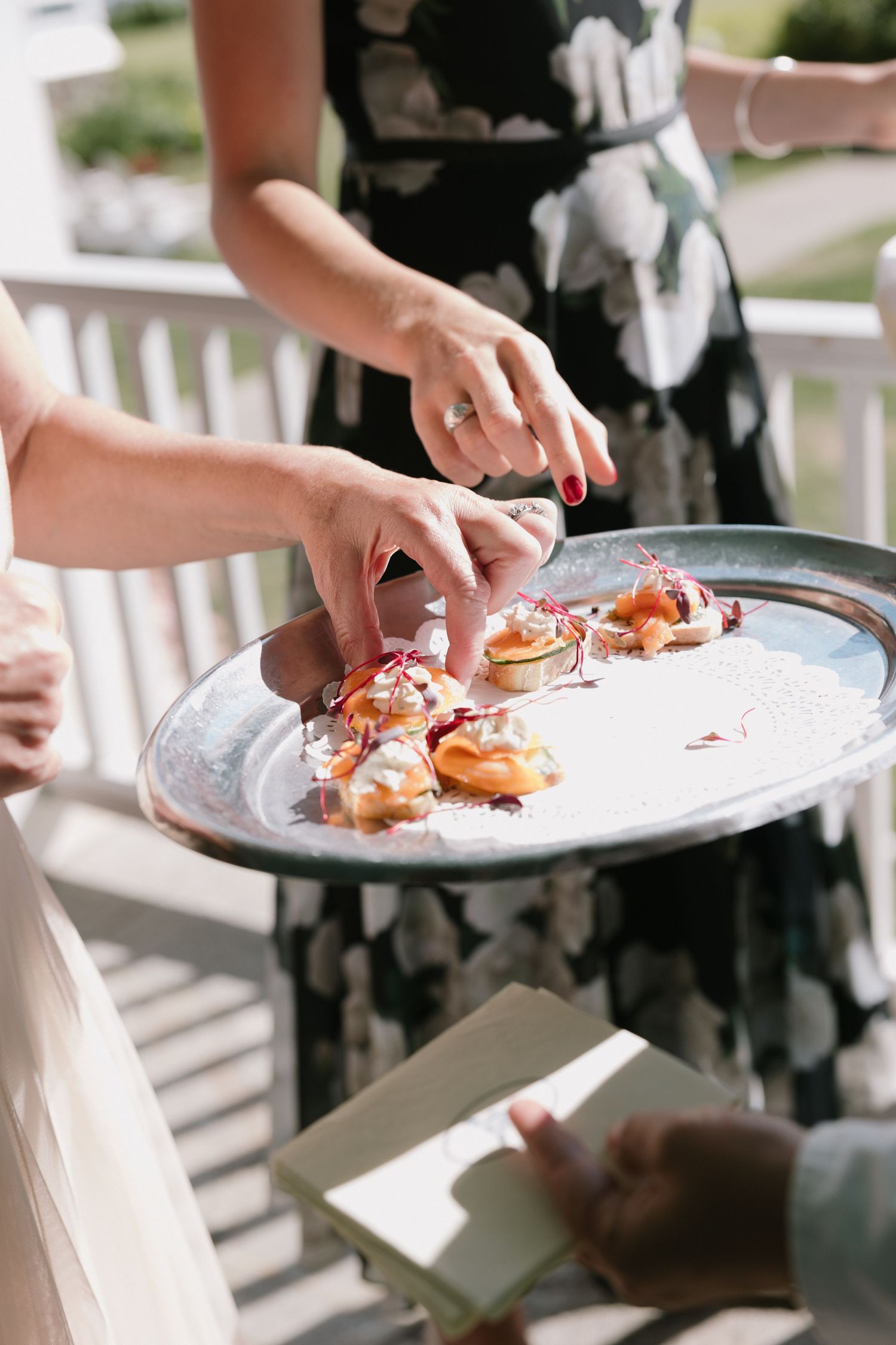 Guests reaching for elegant appetizers on a silver tray at an outdoor catered event.