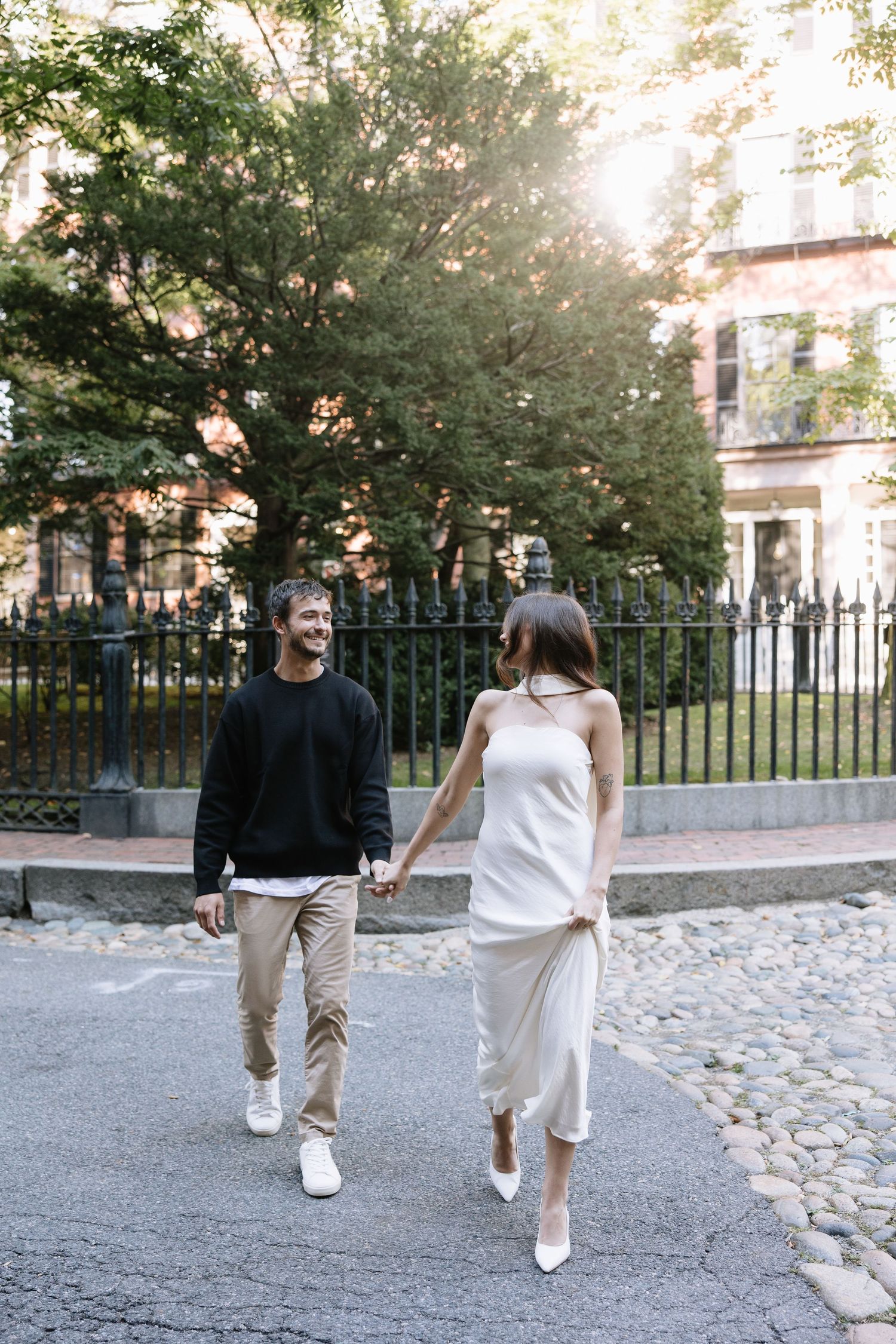 Couple walking hand in hand on a tree-lined street wearing contrasting black and white outfits.