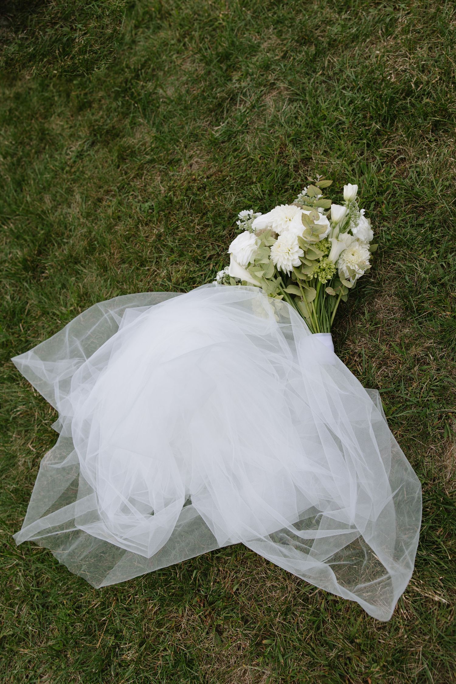 White wedding veil and floral arrangement laying on green grass.