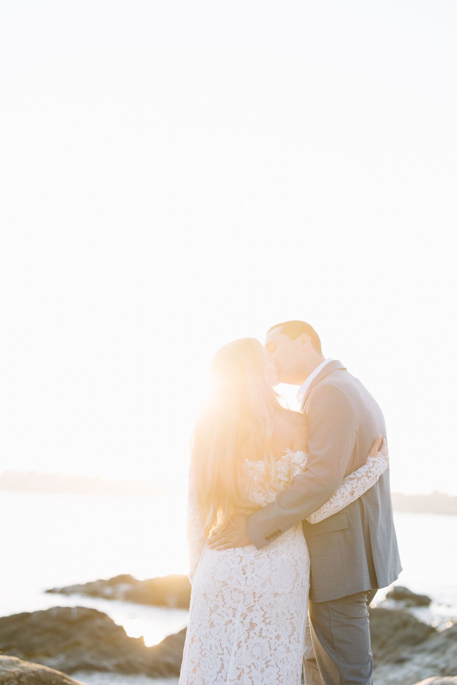 Silhouetted couple embracing against bright sunset over water.
