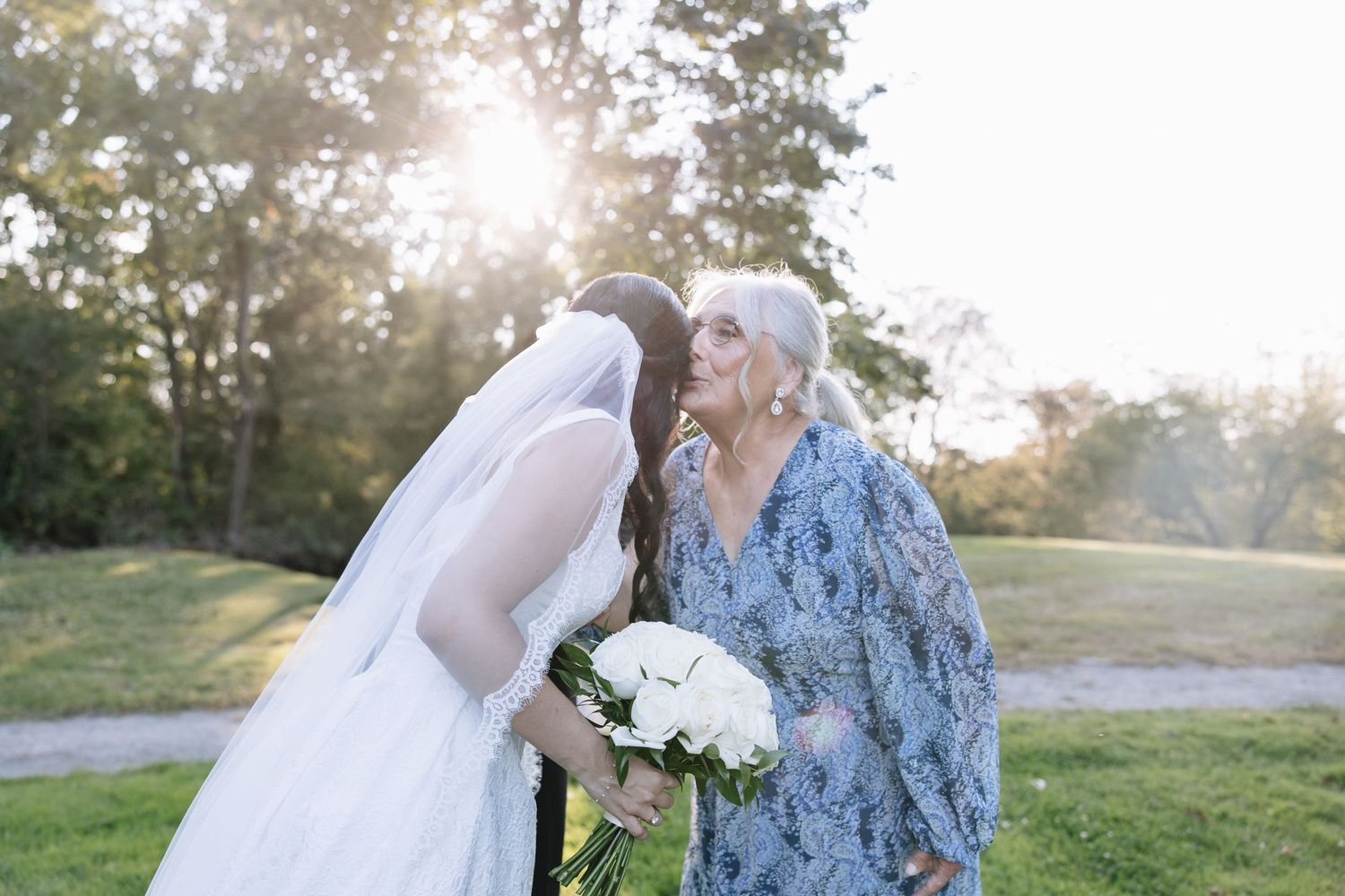 Intimate wedding moment captured in golden sunlight with white floral bouquet.