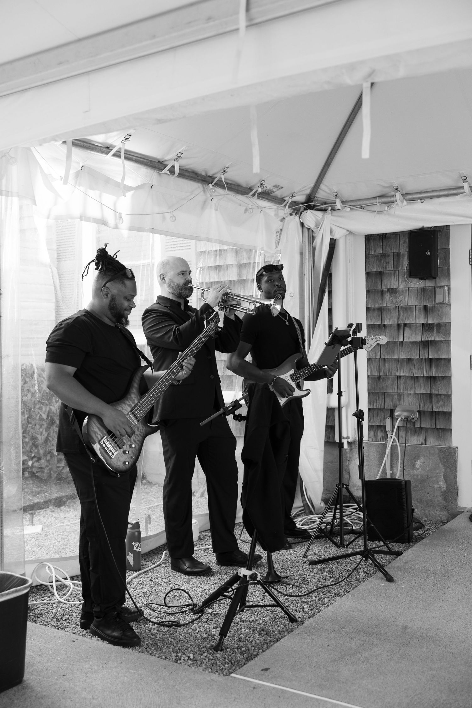 Black and white photo of live band performing under wedding reception tent.