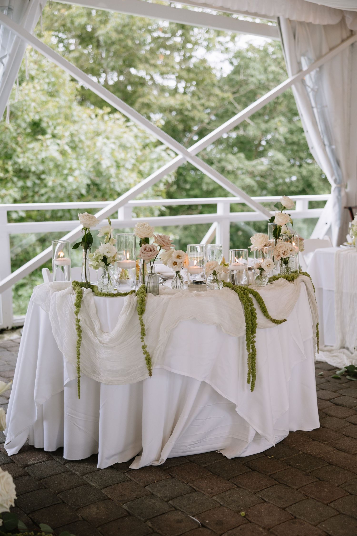 White wedding reception tables decorated with floral centerpieces and greenery garlands.