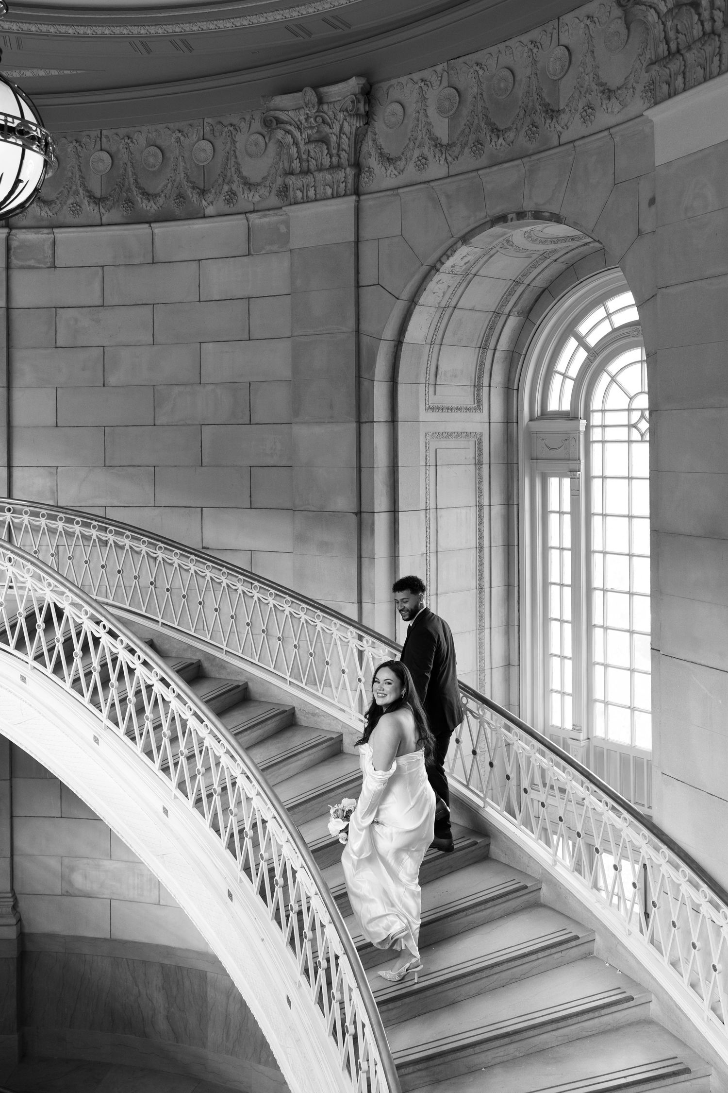 Black and white photo of couple ascending grand marble staircase.