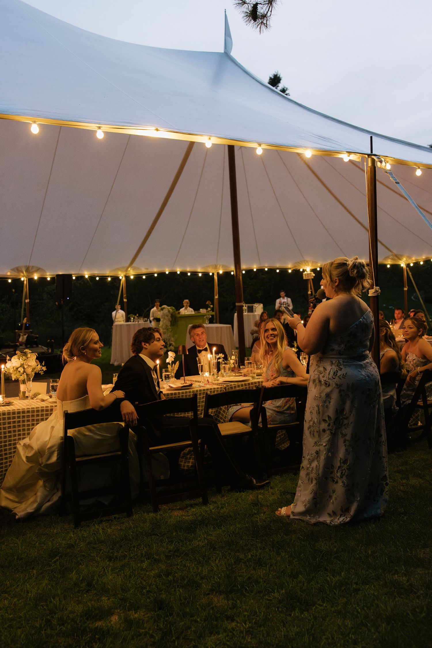 Large white wedding tent with string lights and guests enjoying an evening reception.