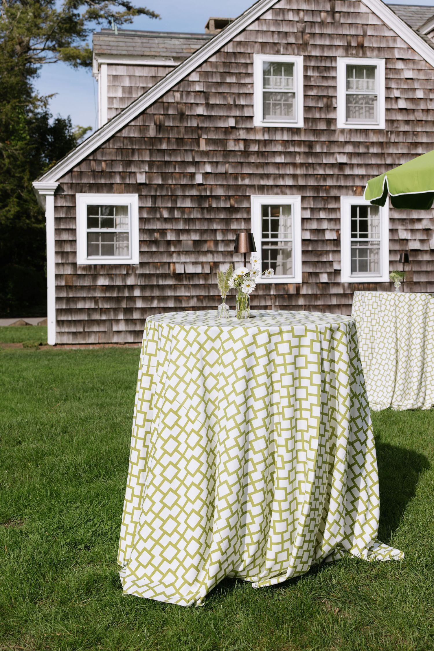 Rustic shingle-sided building with green and white patterned tablecloths set up outdoors.