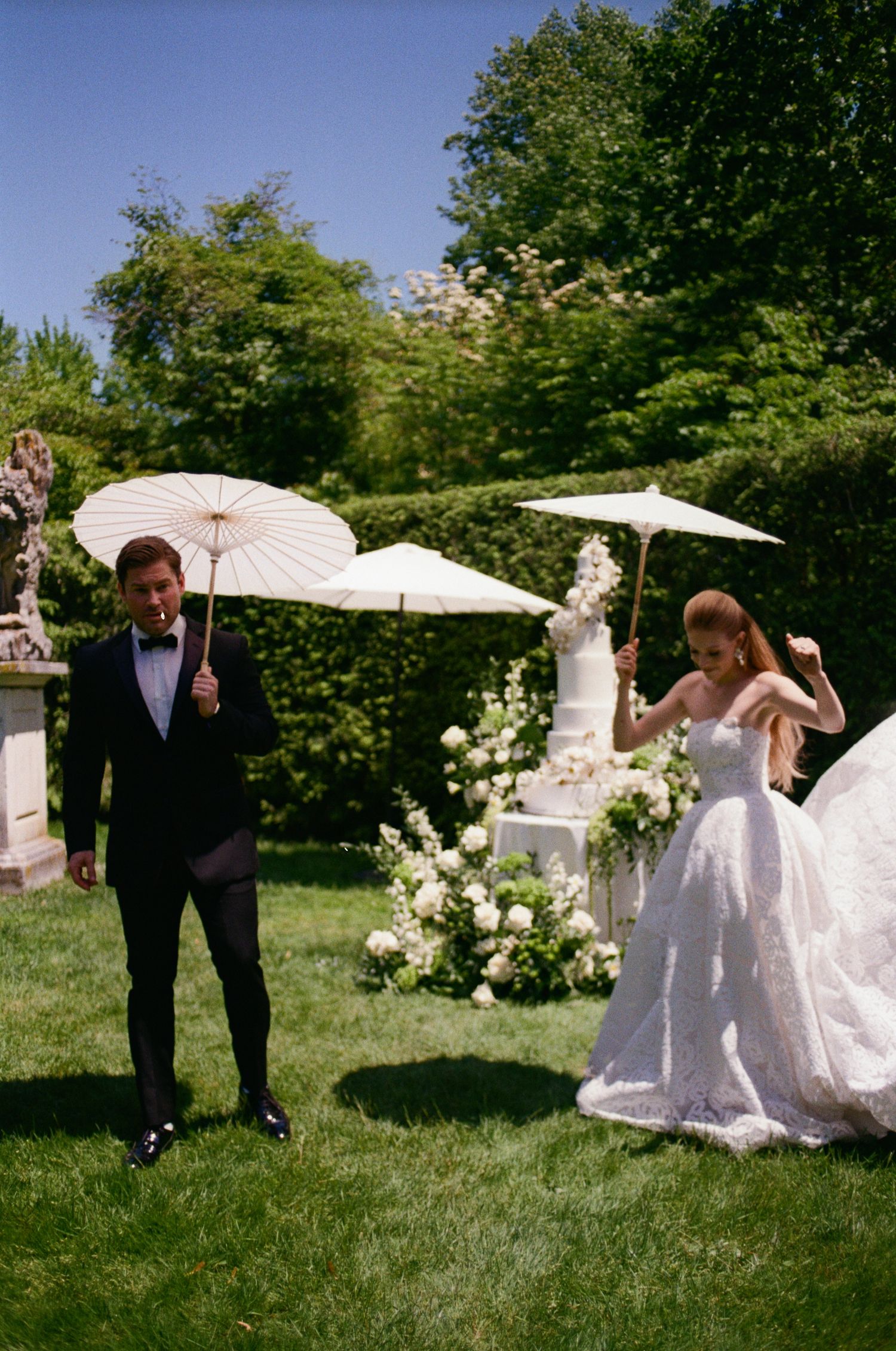 Wedding couple posing with white parasols in a lush garden setting.