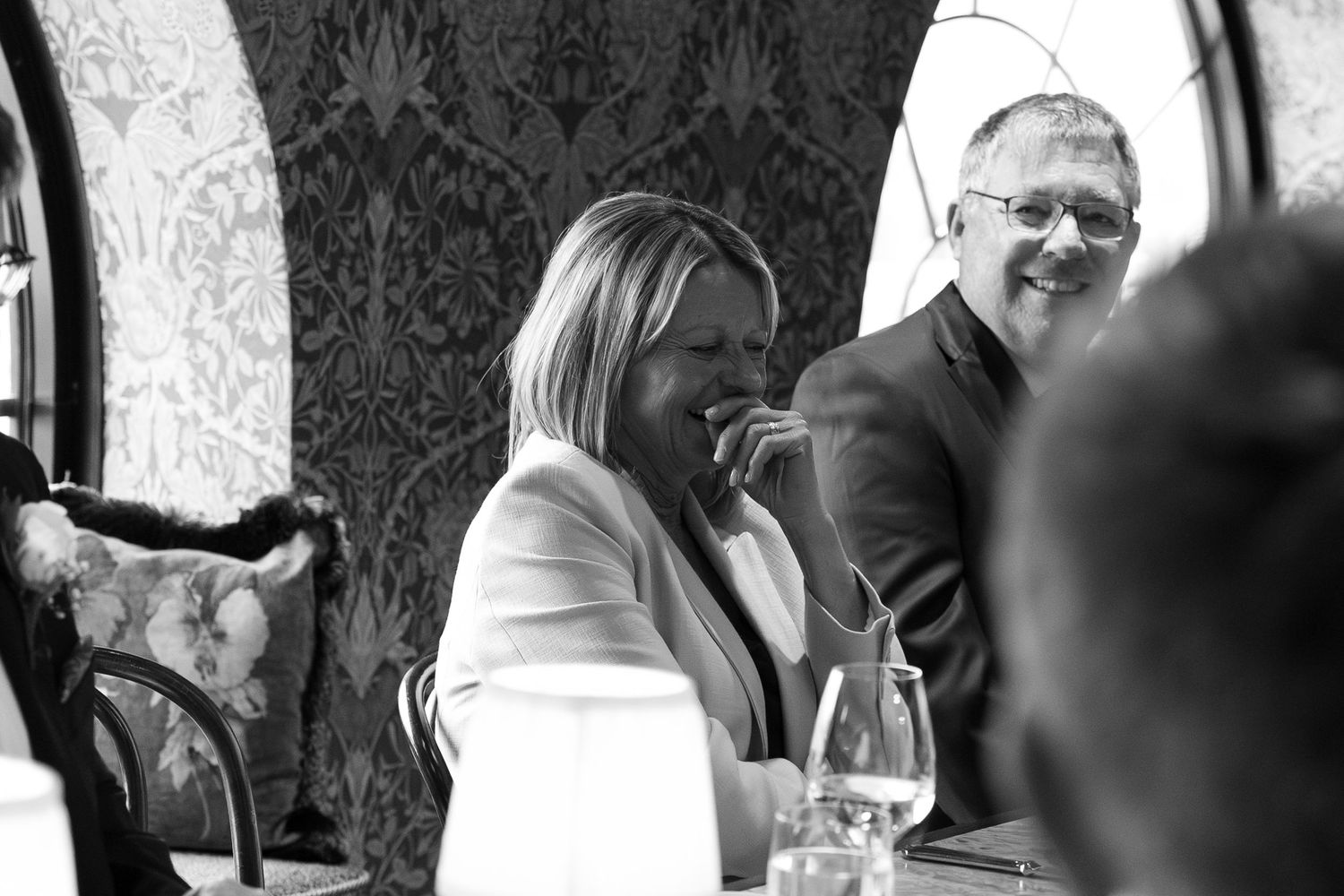 Black and white photo of a smiling couple at a restaurant table with wine glasses.