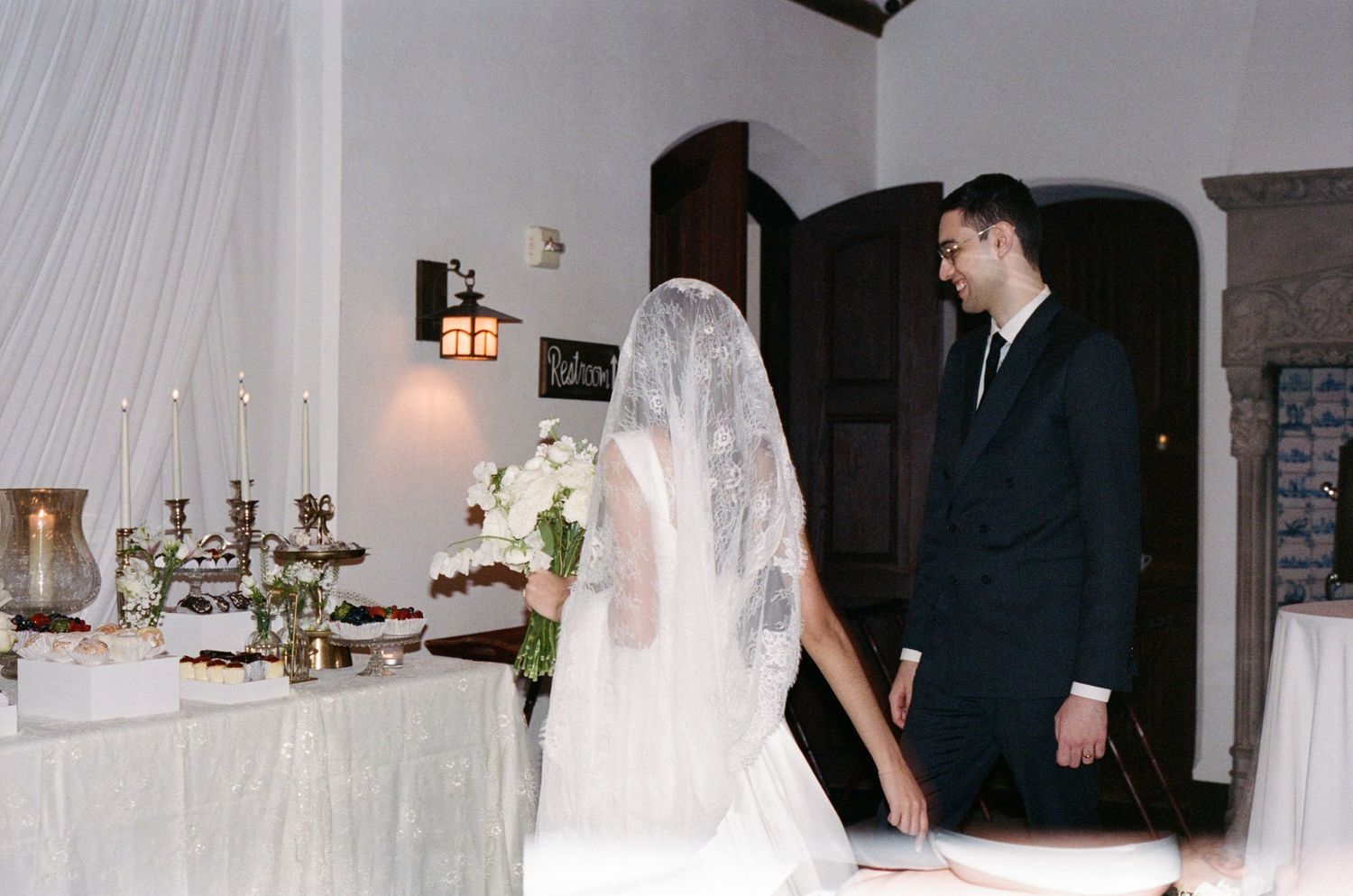 Bride and groom standing at decorated wedding altar with white floral arrangements and candles in elegant venue.