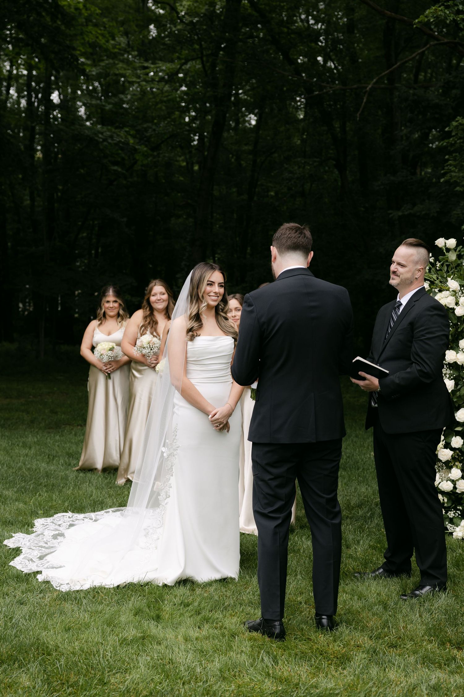 Outdoor wedding ceremony with couple and wedding party at floral-decorated altar.