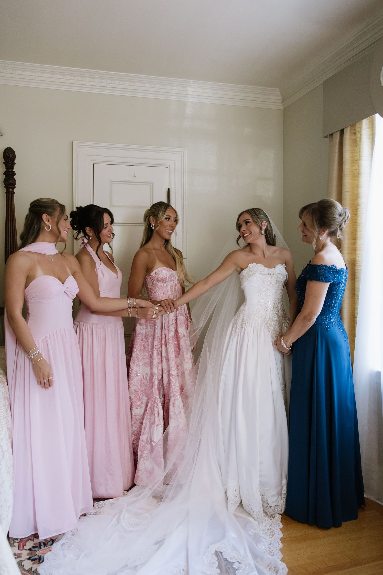 Wedding party in pink and blue dresses helping with the bride's gown.