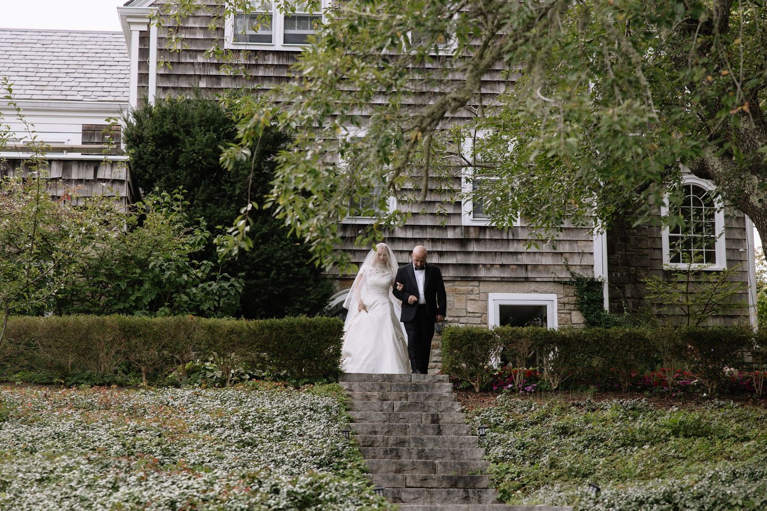 Couple walks down stone path in front of classic New England style house.