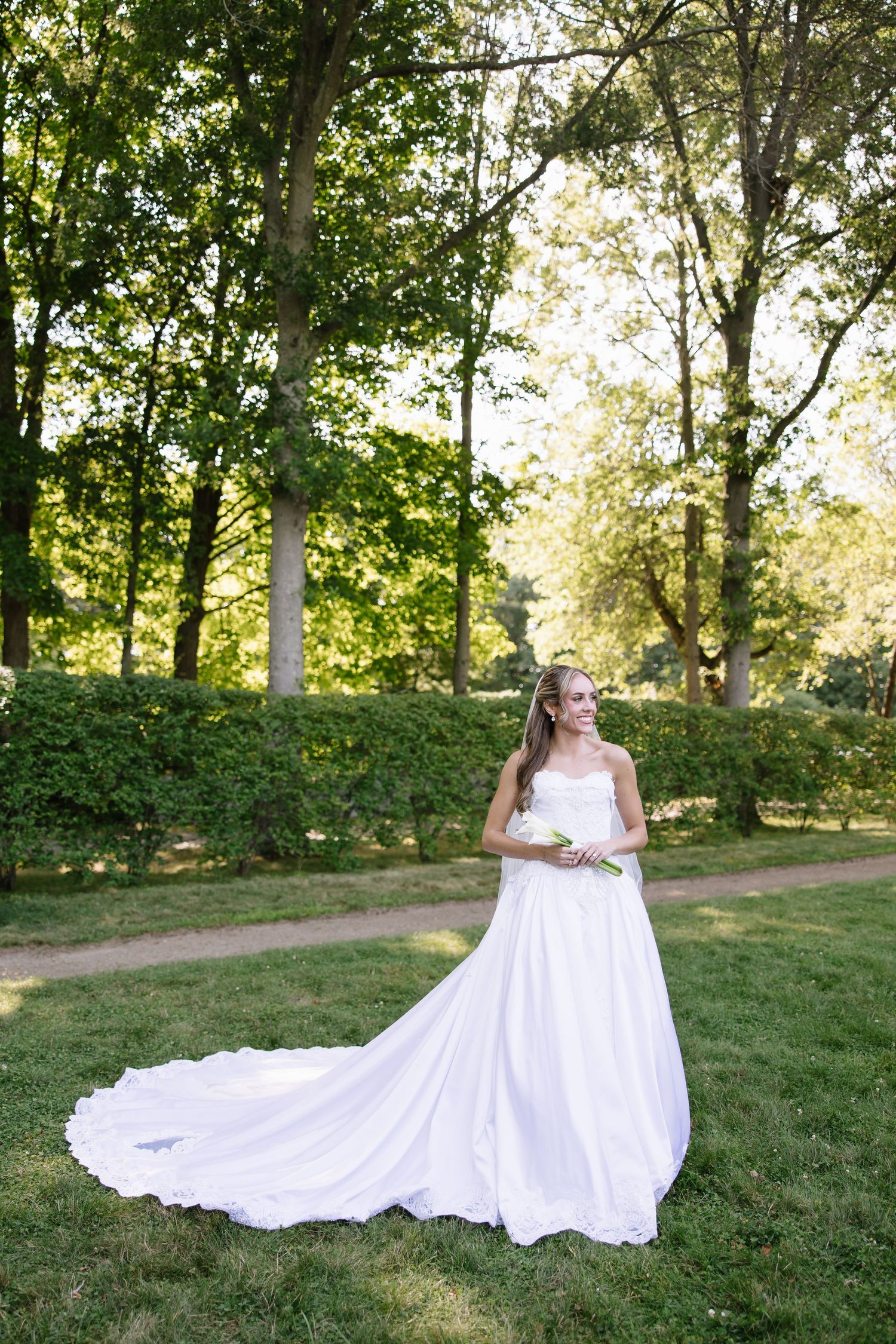 Classic white wedding gown with long train photographed on sunny garden lawn.