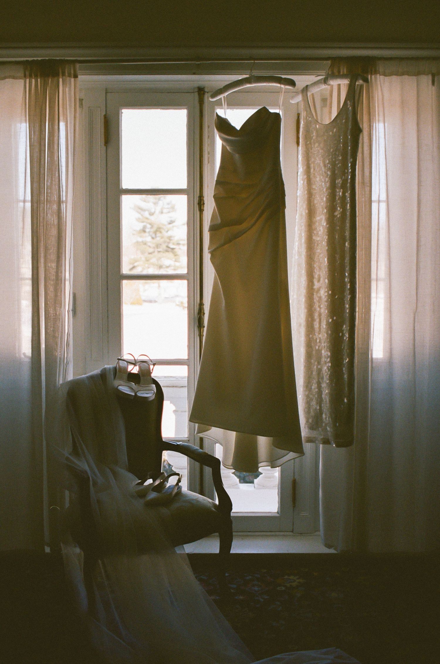 Elegant bridesmaid dresses hanging by windows in preparation for a wedding day.