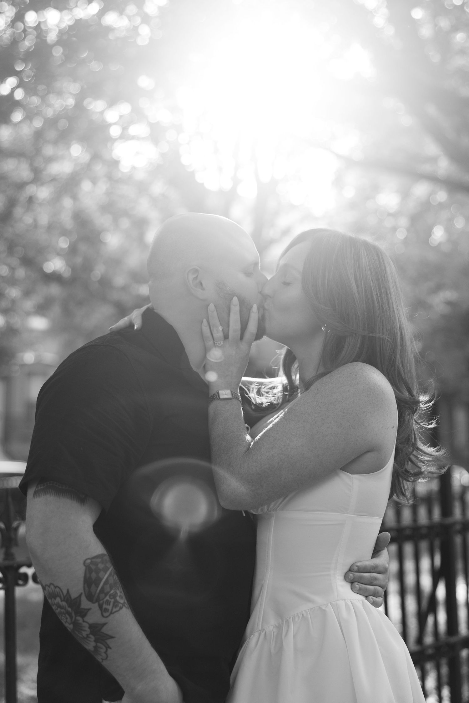 Black and white photo of intimate moment between couple with sun flare in background.
