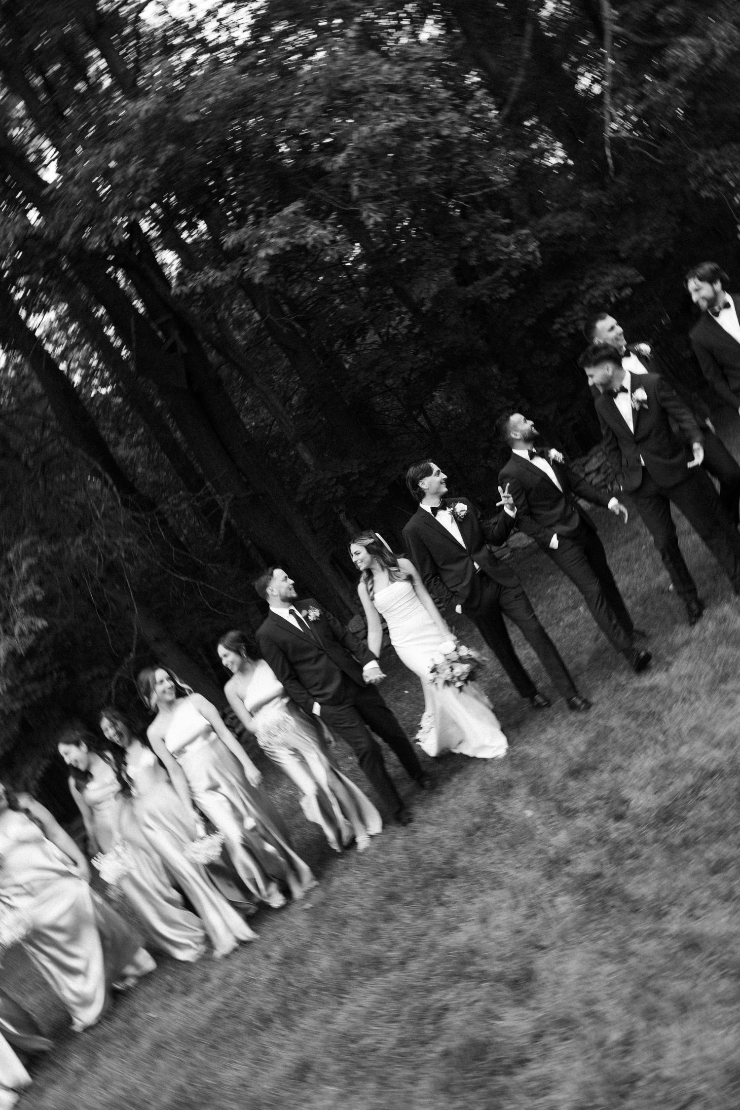 Wedding party walks together across grassy hill in black and white photo.