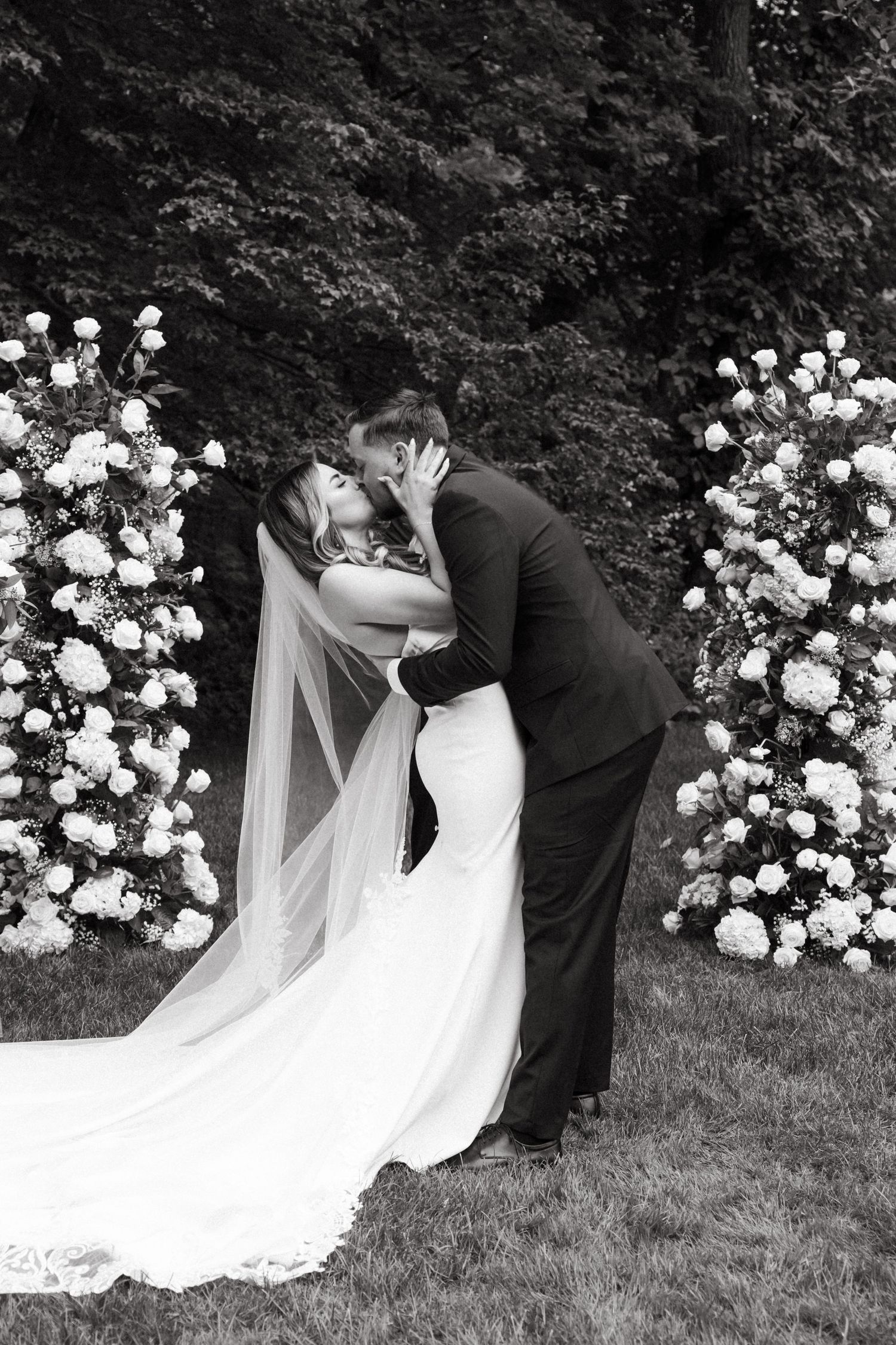 Black and white photo of a wedding ceremony with white floral decorations in a garden setting.
