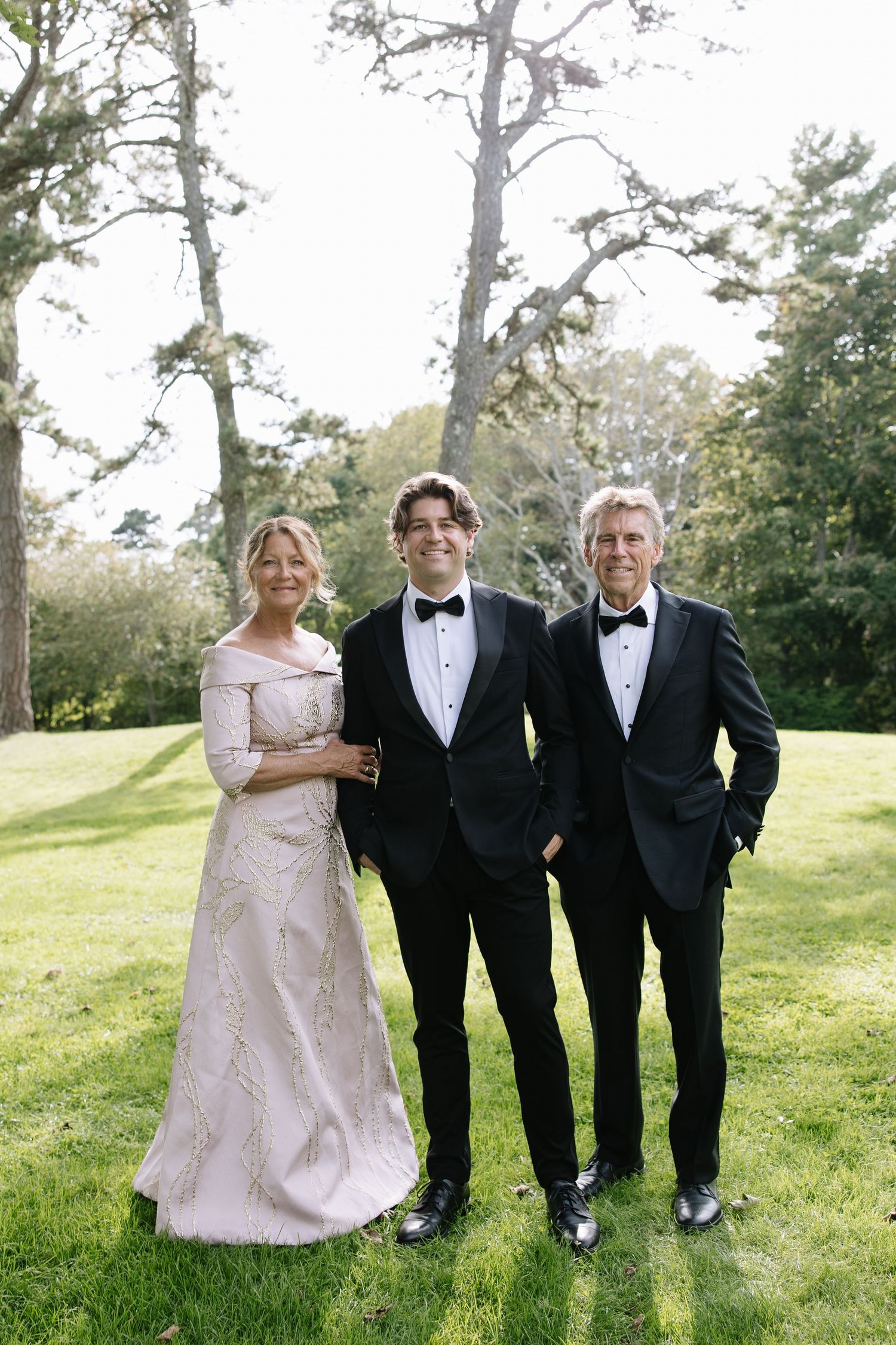 Wedding party in formal attire posing on grassy hillside.