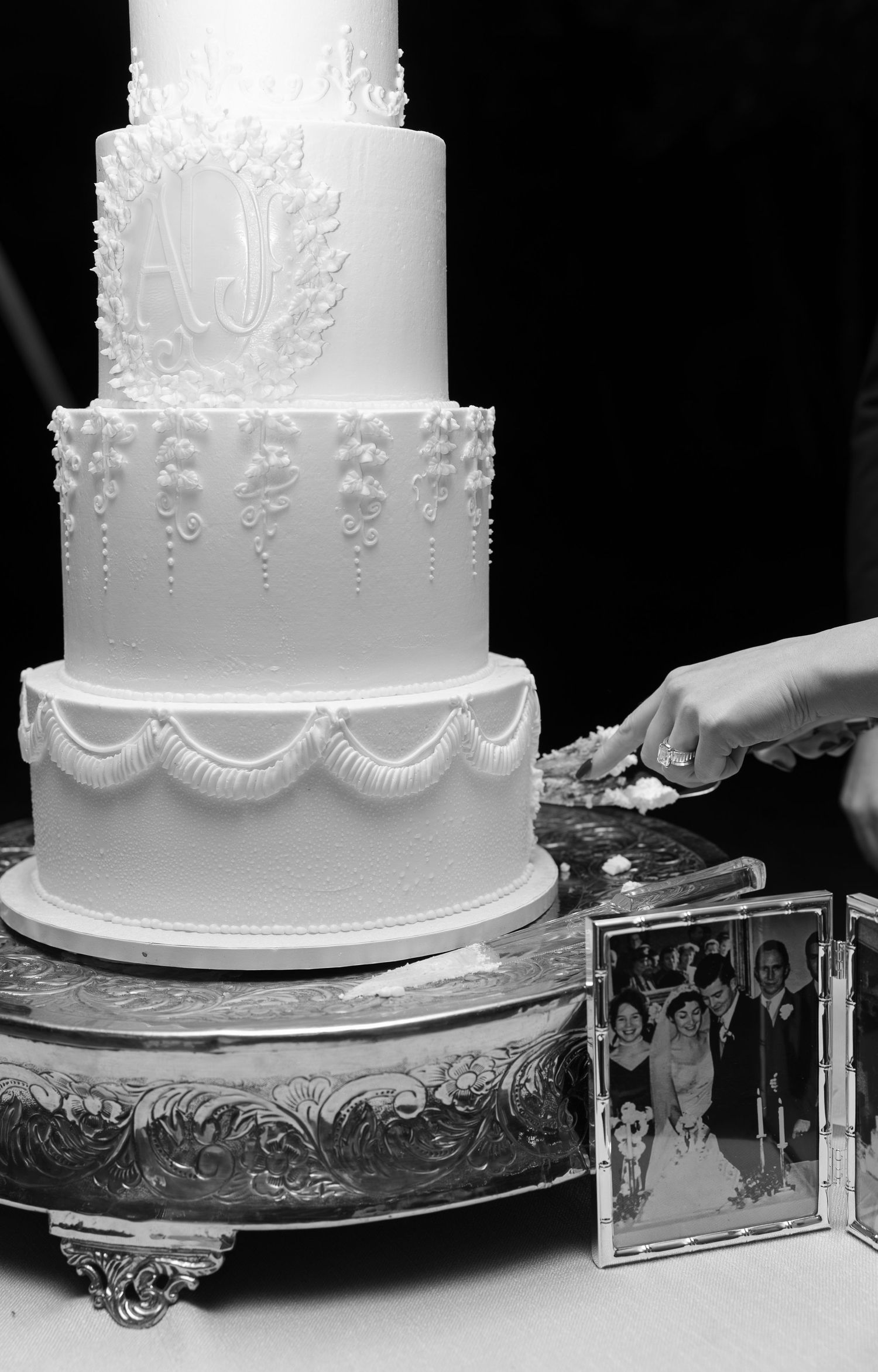 Elegant white wedding cake with detailed lace piping and scalloped edges on a silver cake stand.