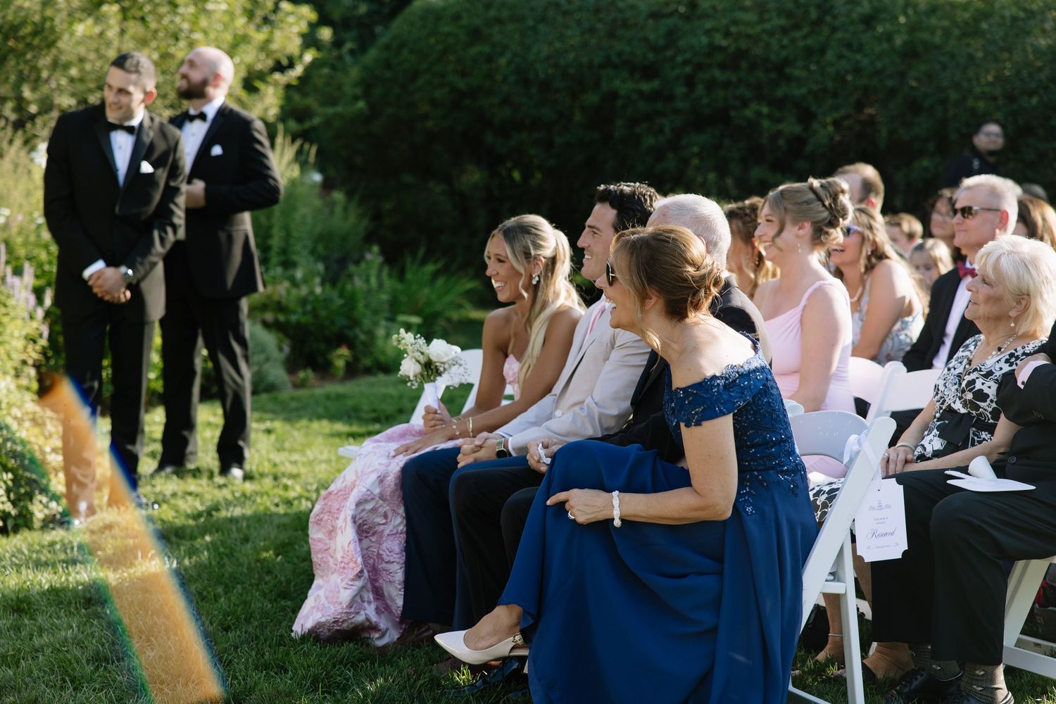 Wedding guests seated in white chairs during an outdoor garden ceremony.