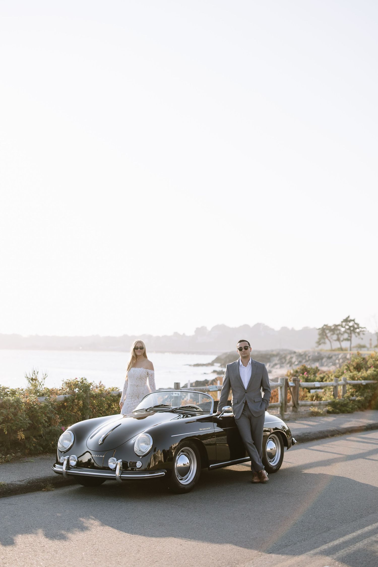 Classic black Porsche Speedster parked on coastal road at sunset.
