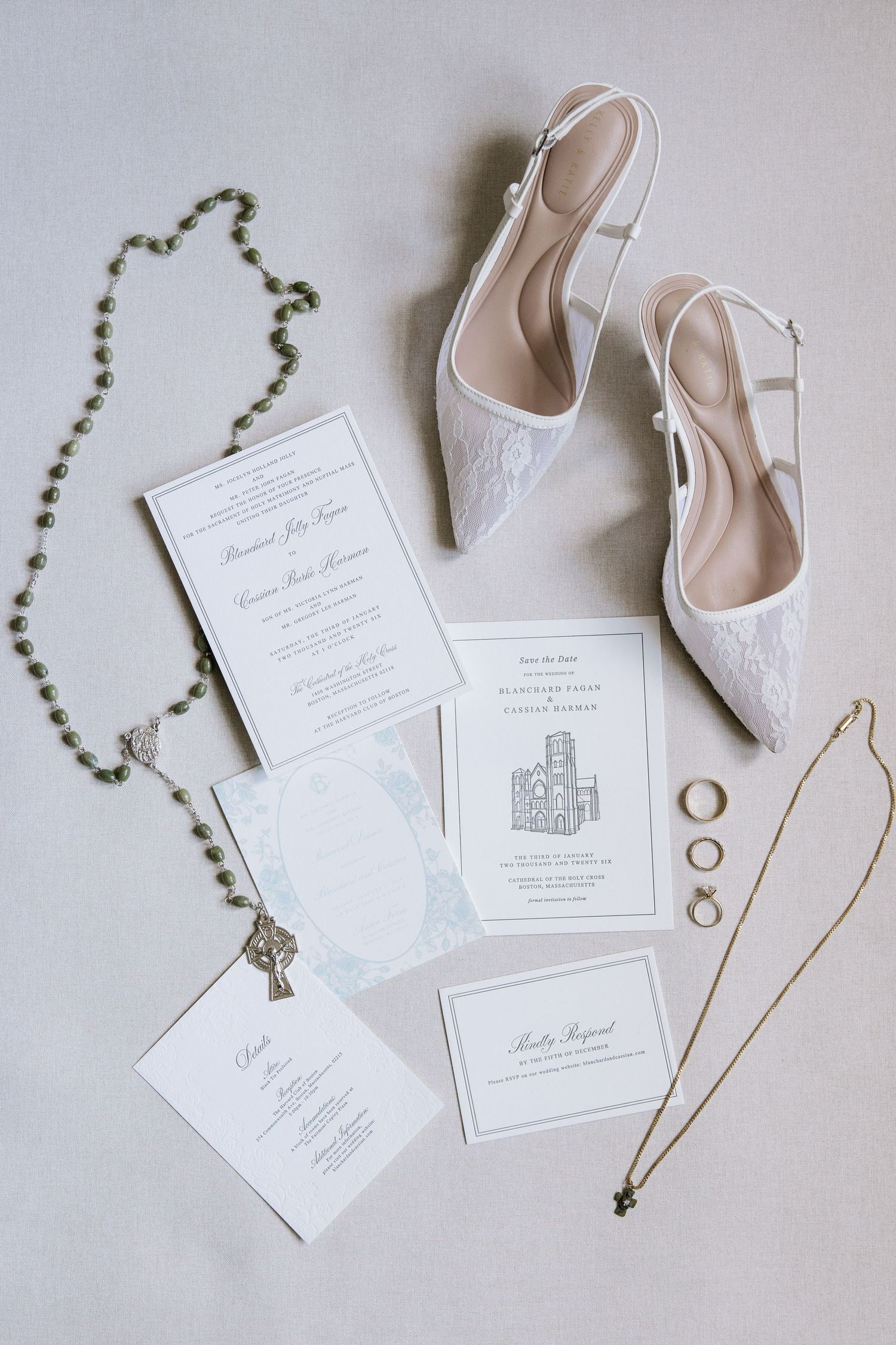 Wedding details flatlay with white invitations, rings, rosary beads and elegant bridal shoes.