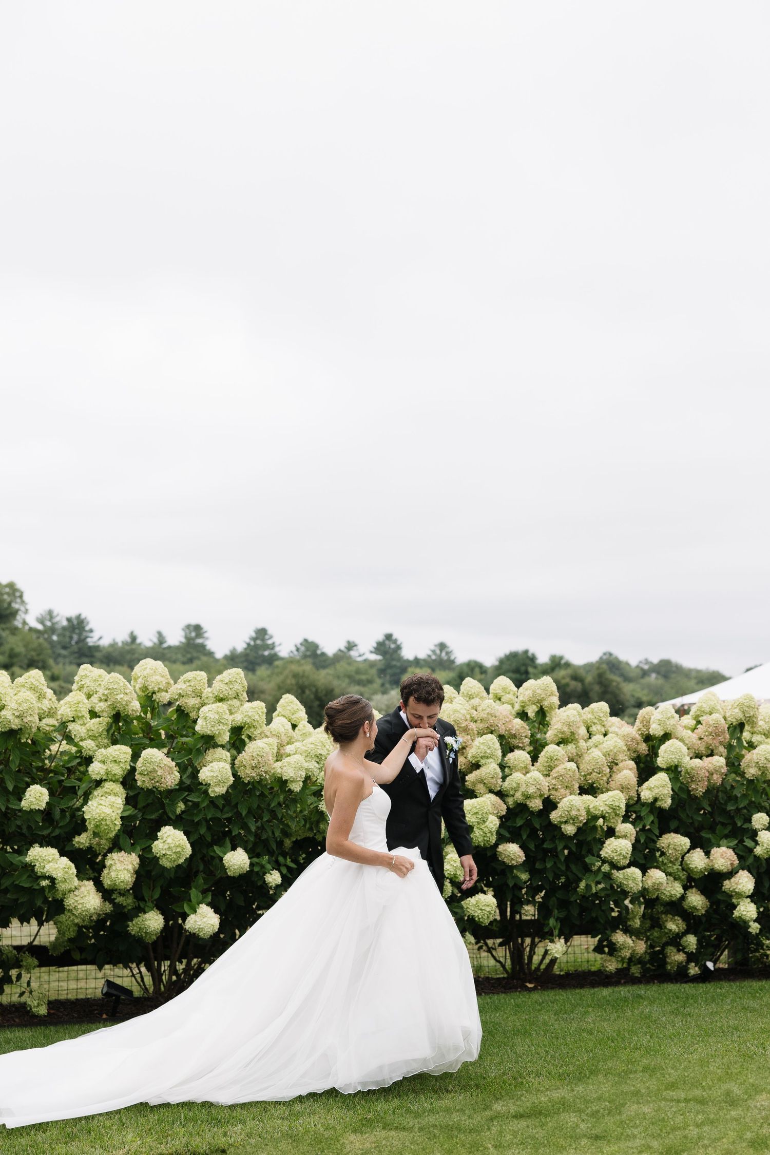 Bride and groom share a romantic dance beside lush white hydrangea bushes during their outdoor wedding ceremony.