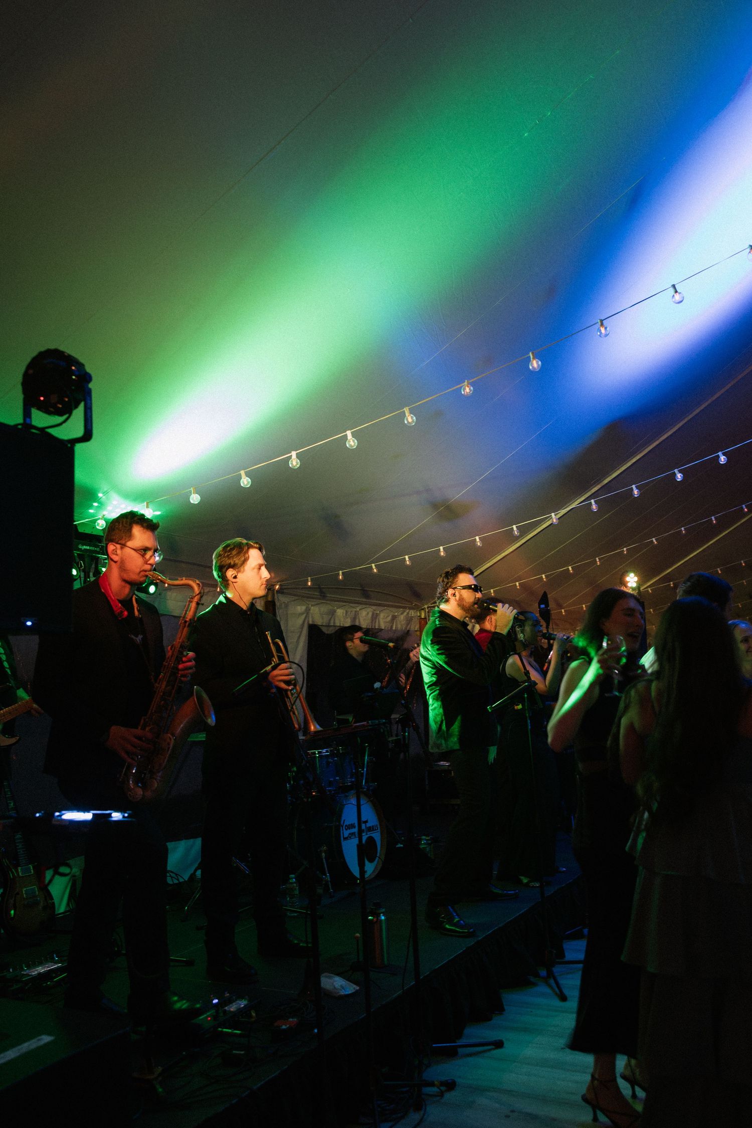 Live wedding band performing on stage under colorful green and blue lights in a festive tent venue.