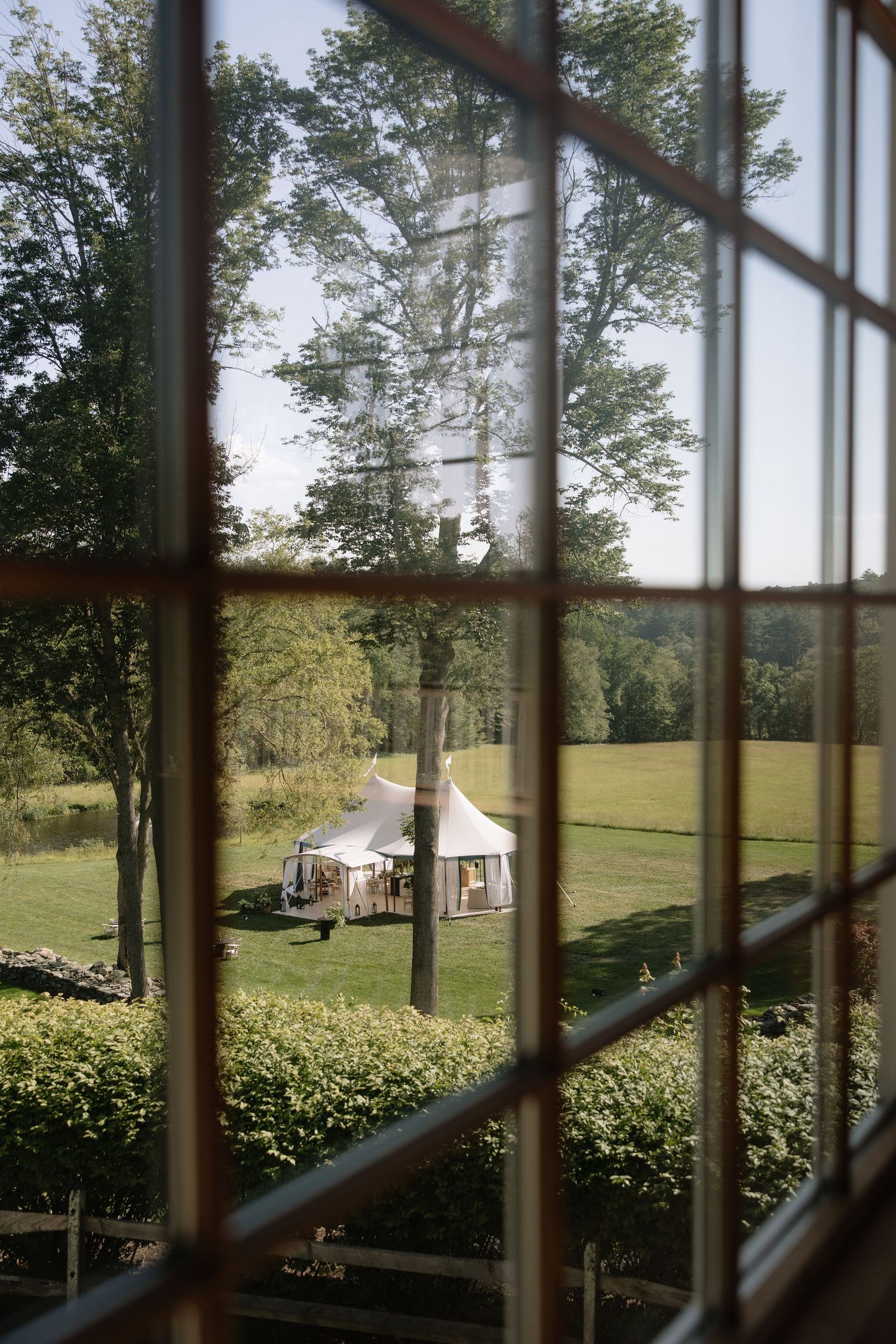 View through vintage window panes of a white wedding tent on a green countryside lawn.