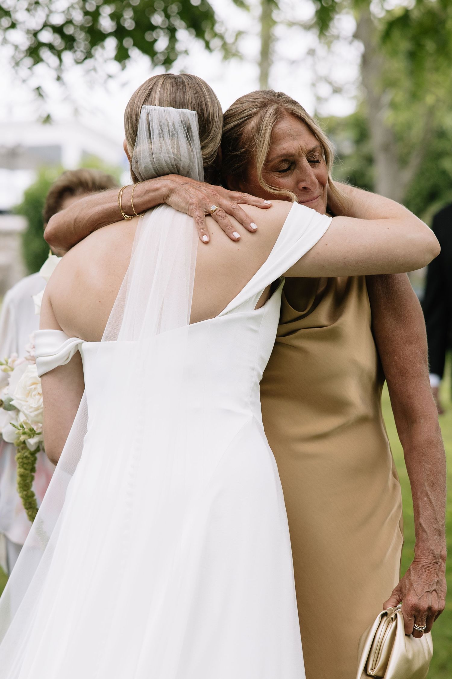 Wedding party members share tender embraces while wearing elegant gold and white dresses.