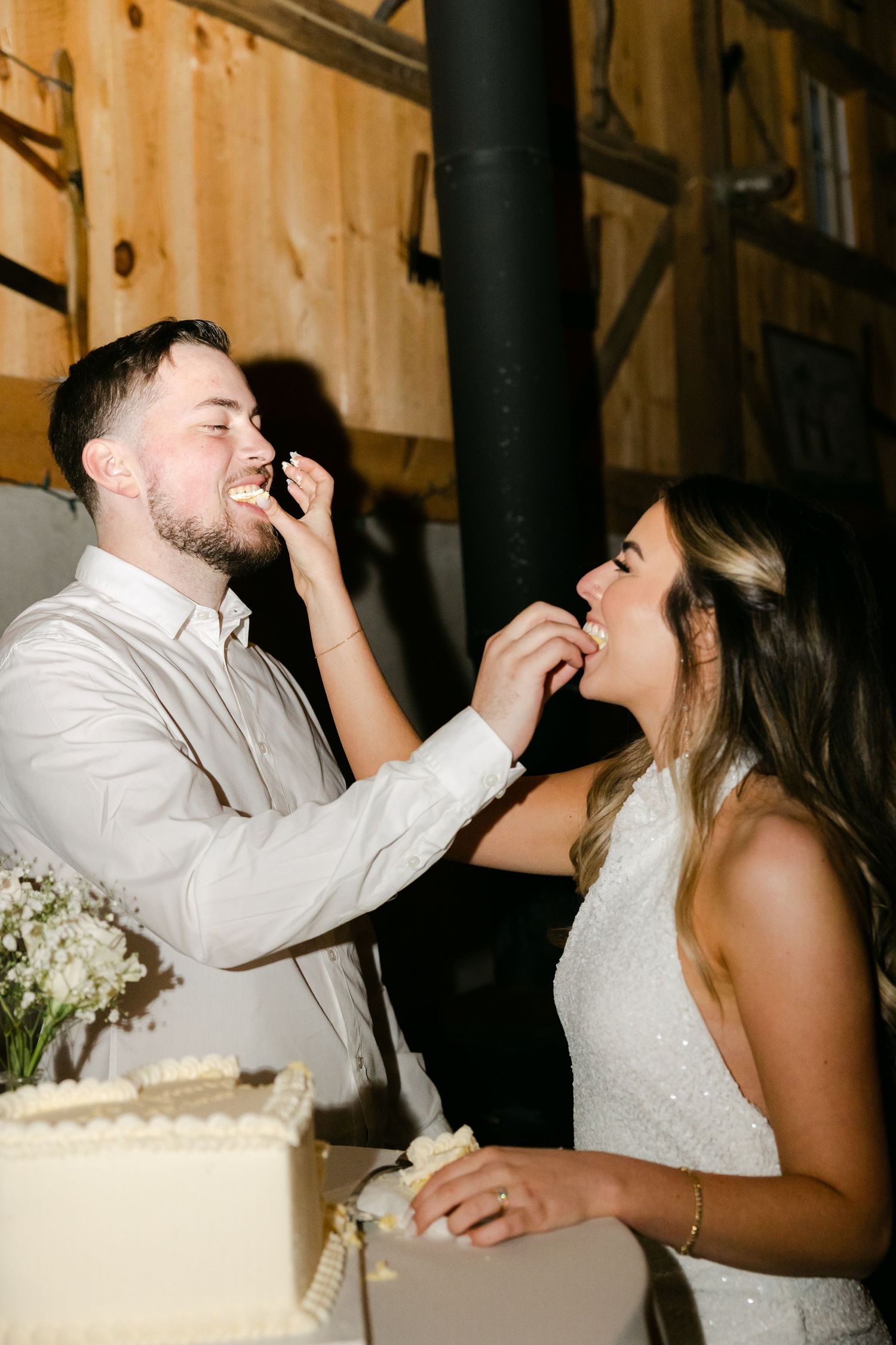Newlyweds playfully feeding each other wedding cake at their reception.
