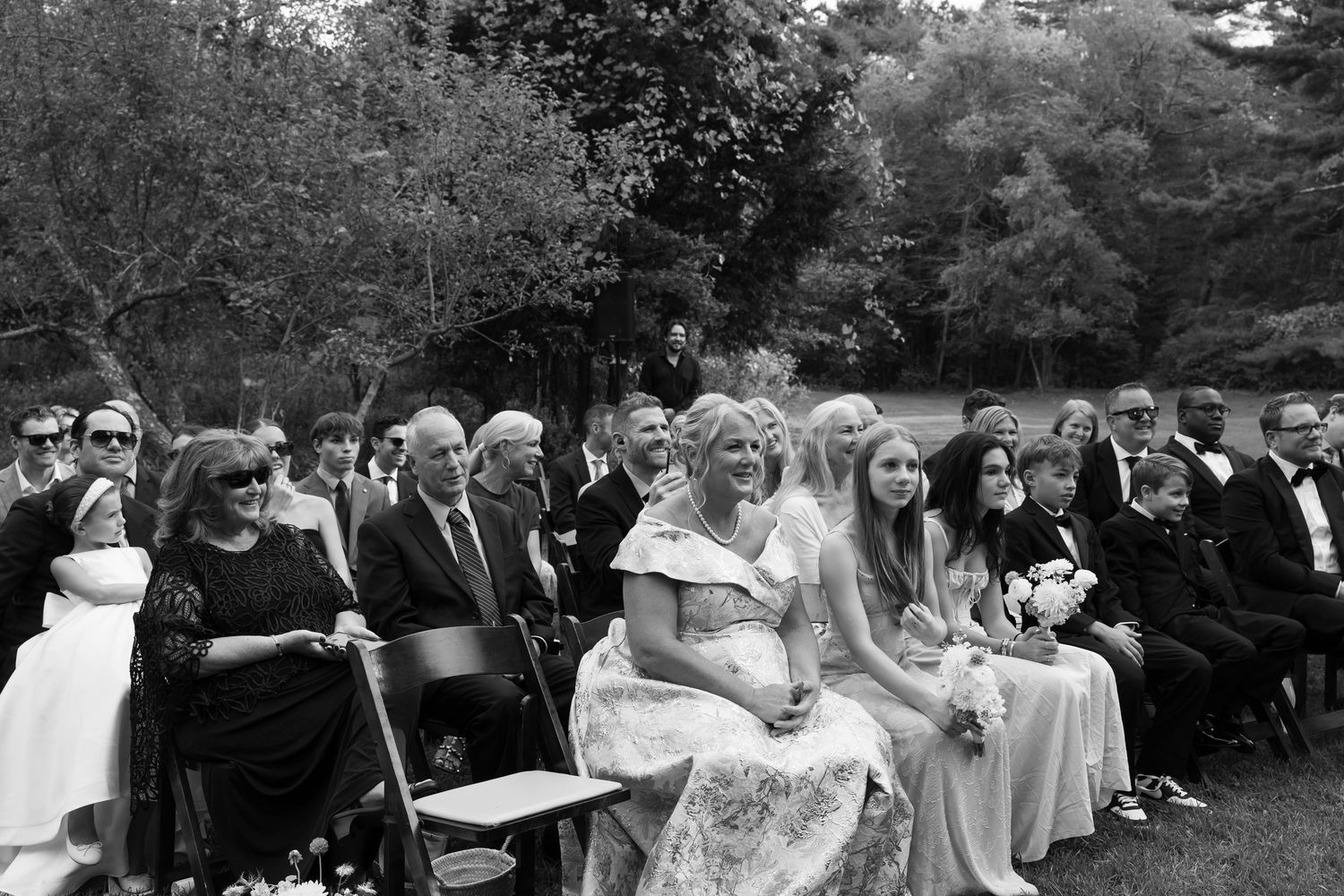 Wedding guests seated in rows watch the outdoor ceremony unfold in a garden setting.