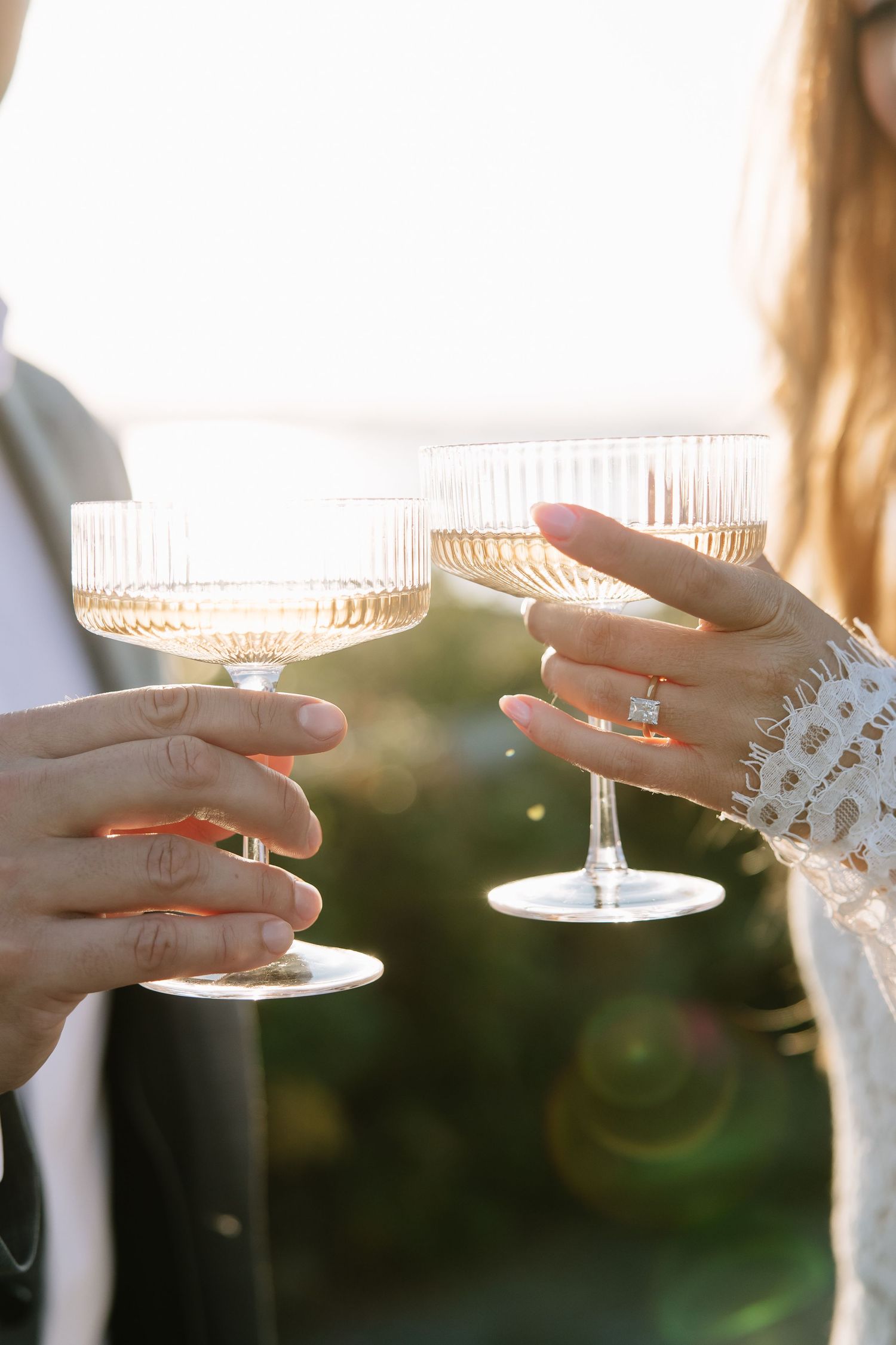 Two hands holding vintage champagne coupes with light filtering through the crystal glassware.