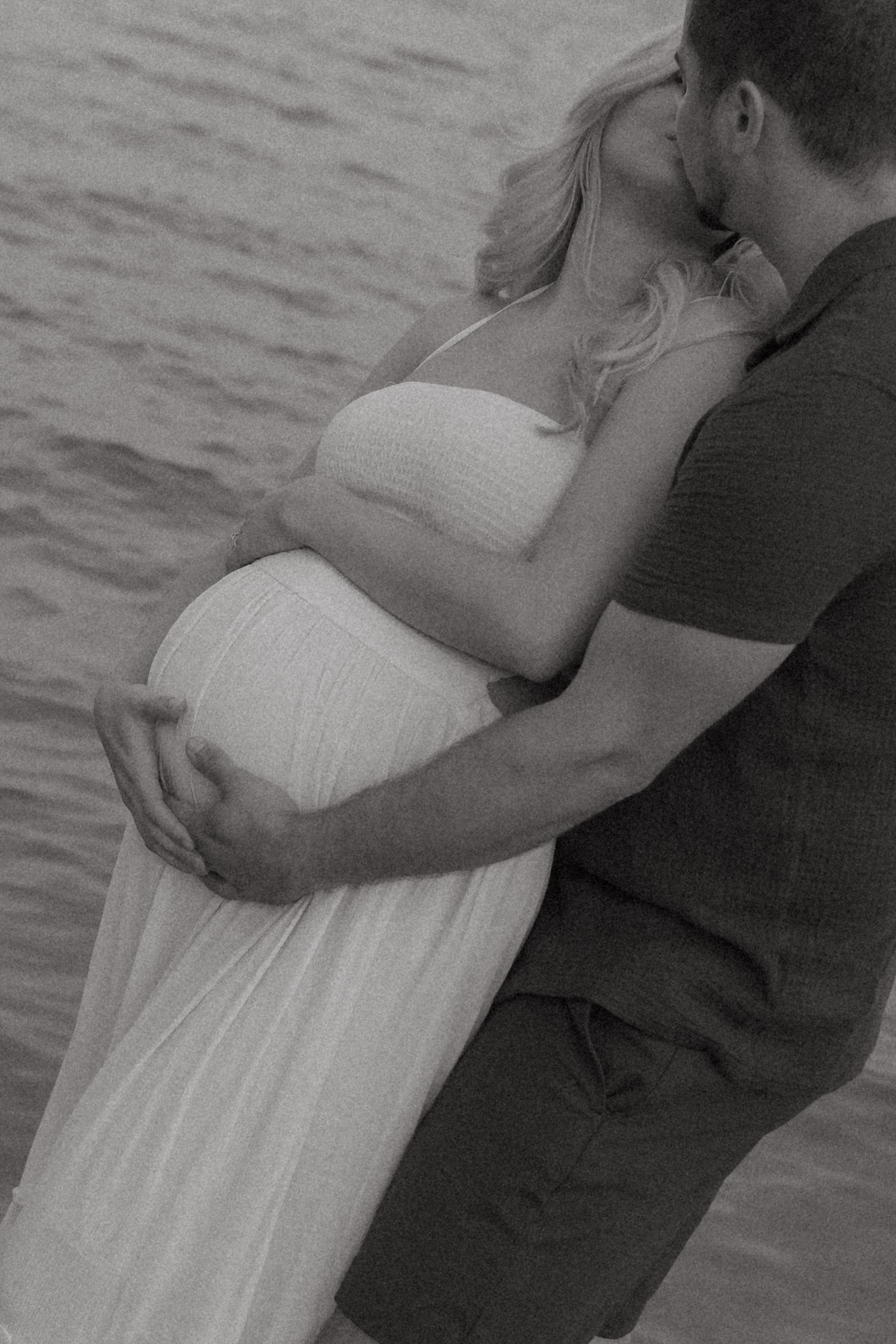 A romantic couple embraces while standing in ocean waves.