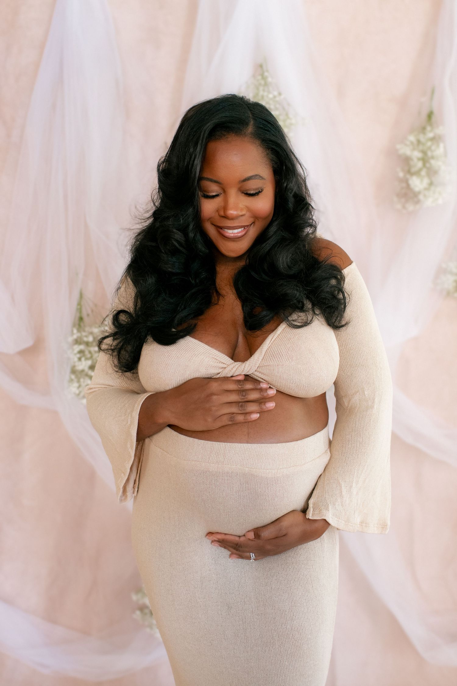 Joyful maternity moment captured against pink fabric backdrop with delicate floral details.