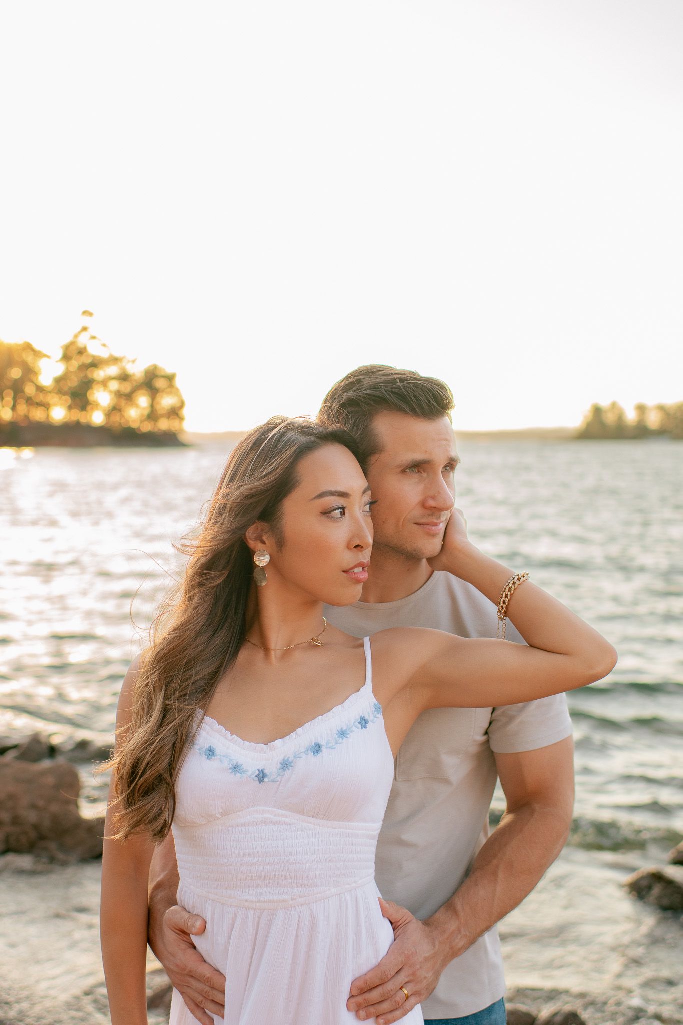 Romantic couple embracing on a rocky beach at sunset with golden light shimmering across the water.